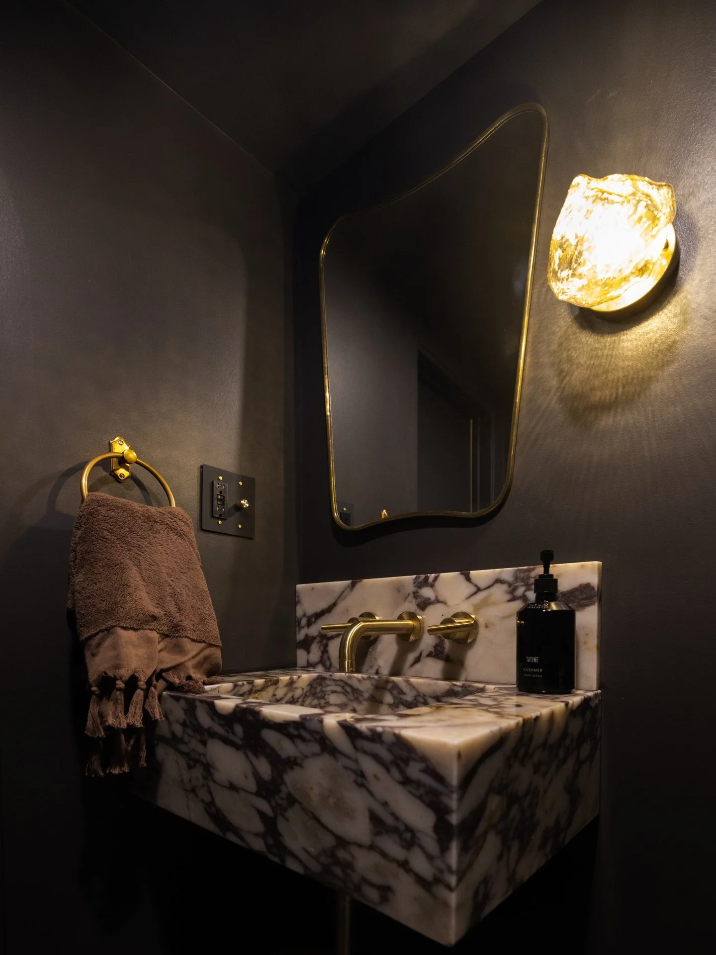 Moody black walls and a marble sink set the tone for a dark-and-sexy basement powder room.  #powderoomdesign #bathroominspo #darkbathroomstyle