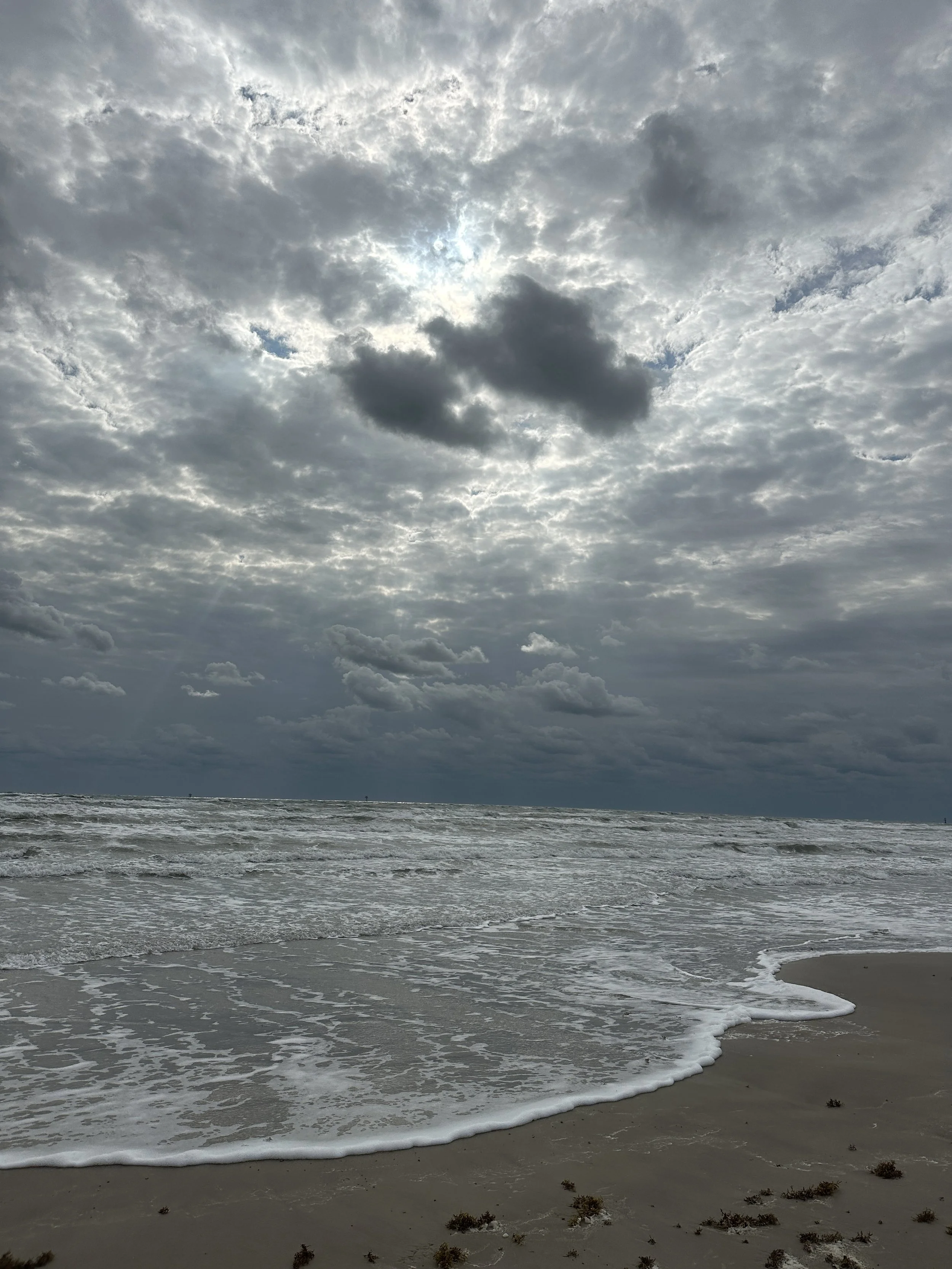 A cloudy sky over a calm ocean with gentle waves reaching the sandy shore.