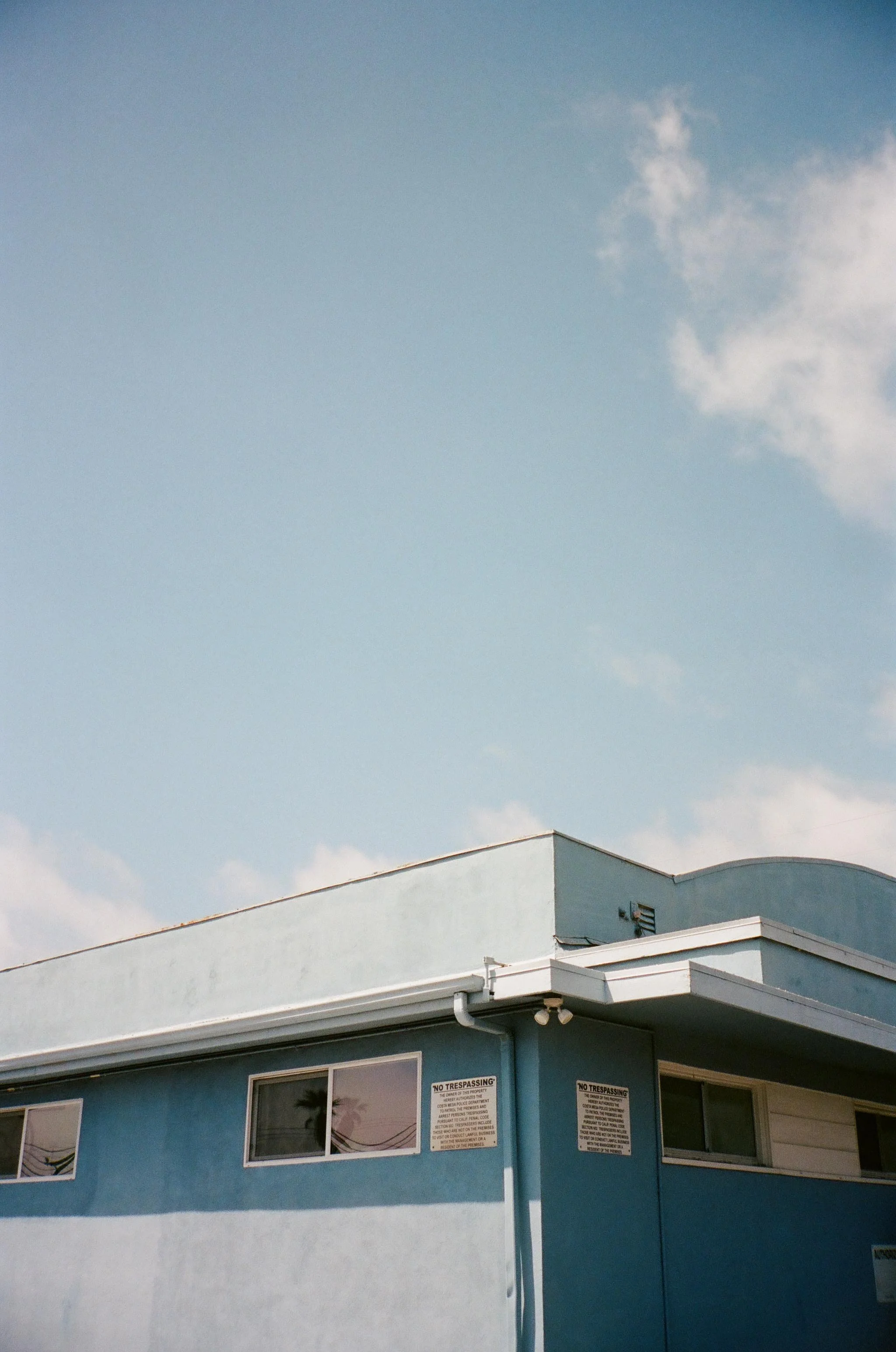 A blue building with multiple windows and 'No Trespassing' signs, set against a partly cloudy sky.