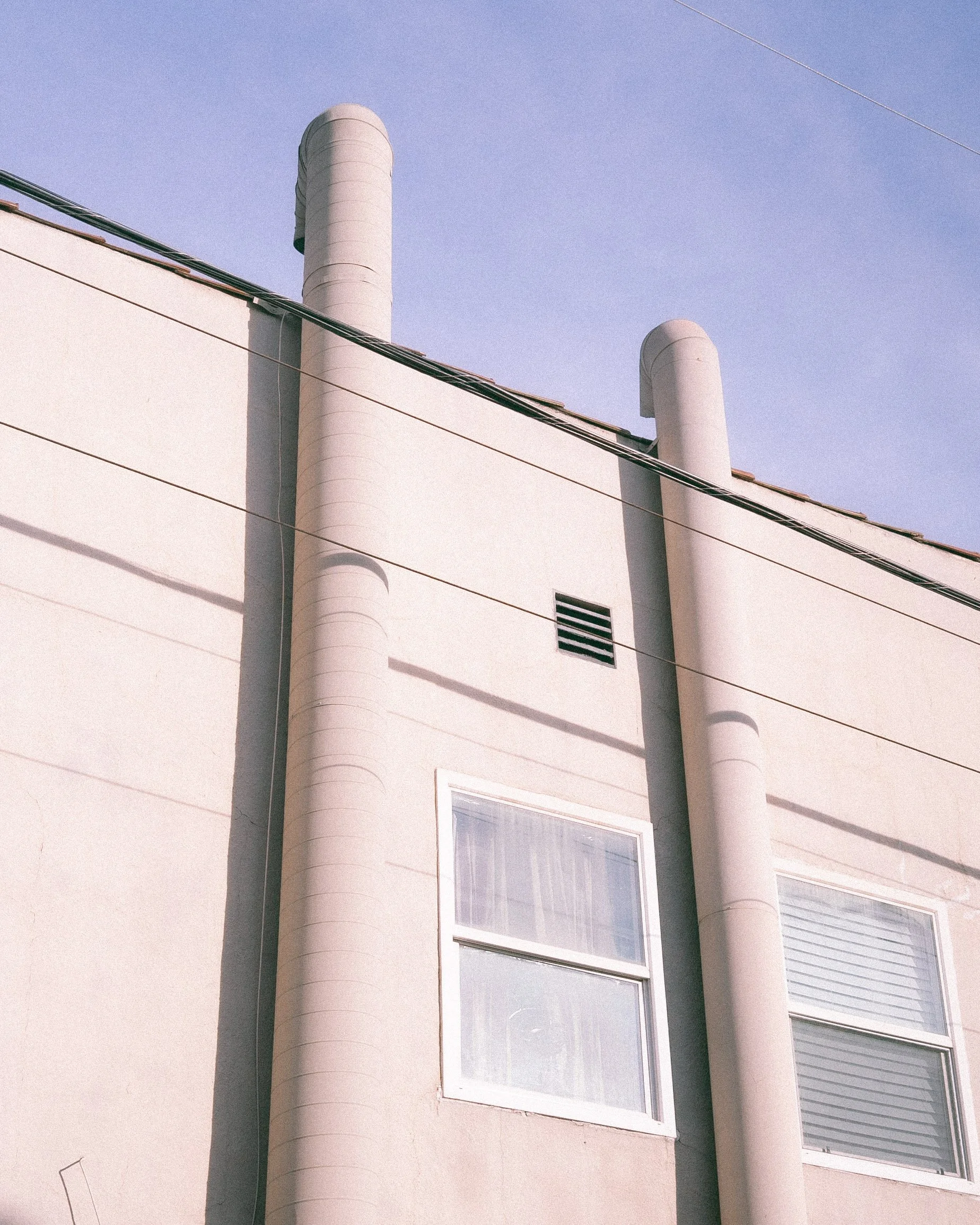 Close-up of a building's exterior with two large white cylindrical structures and several windows, against a clear sky.