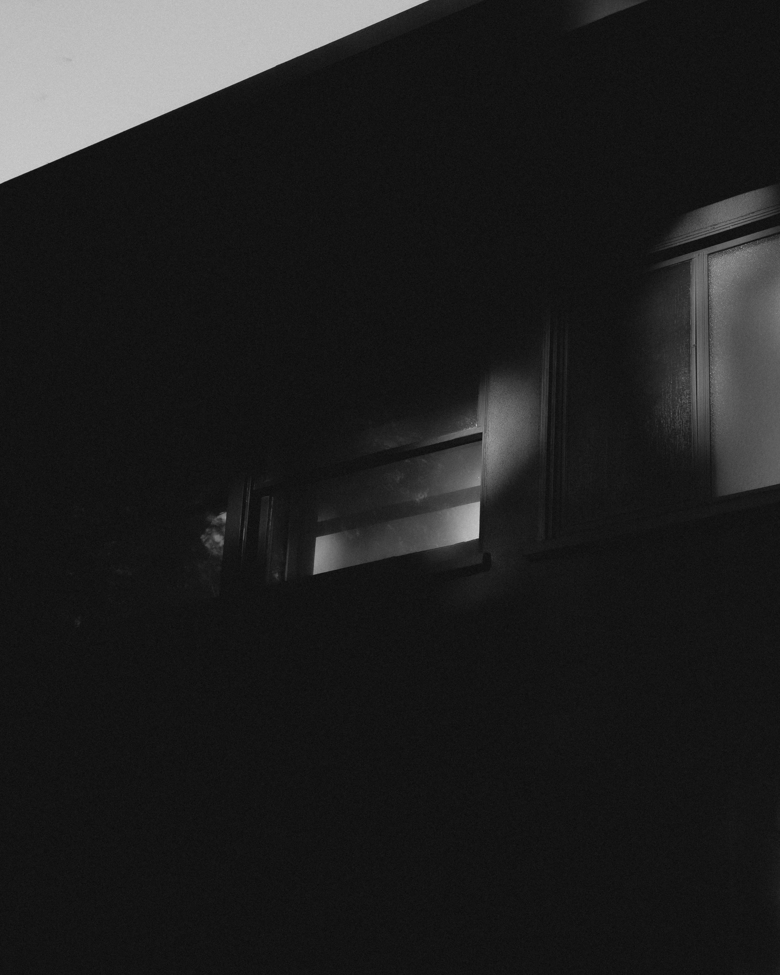 Black and white photo of a building window, partially obscured by shadows.