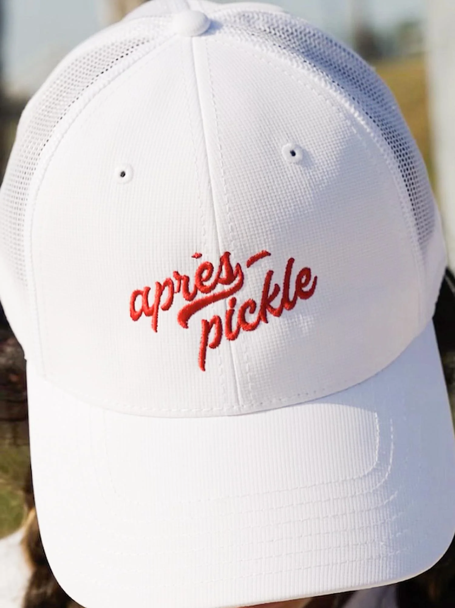 A white baseball cap with the words 'après pickle' embroidered in red on the front.