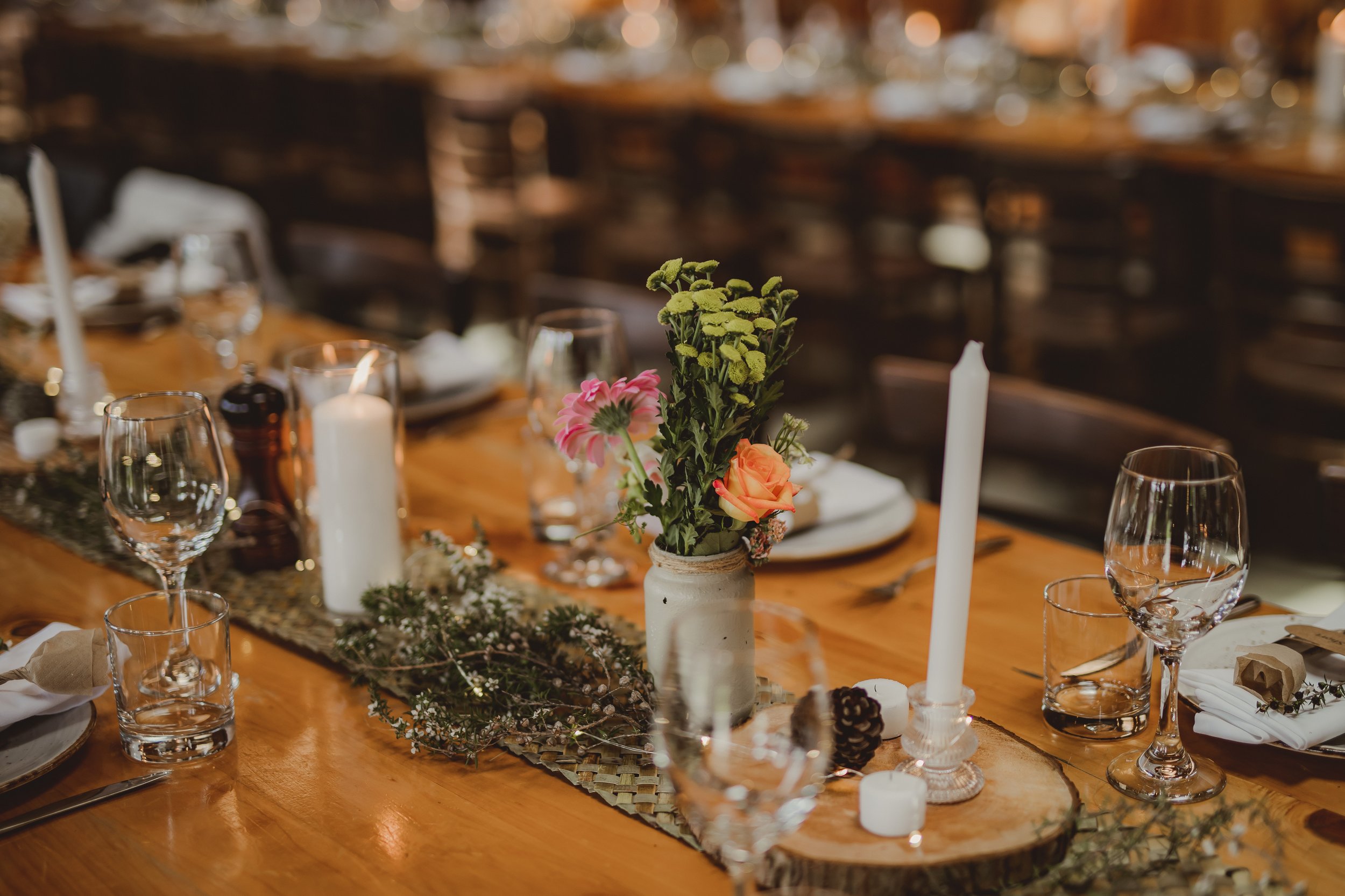A decorated dining table with a wooden centerpiece, floral arrangement, candles, and glassware for a formal event.