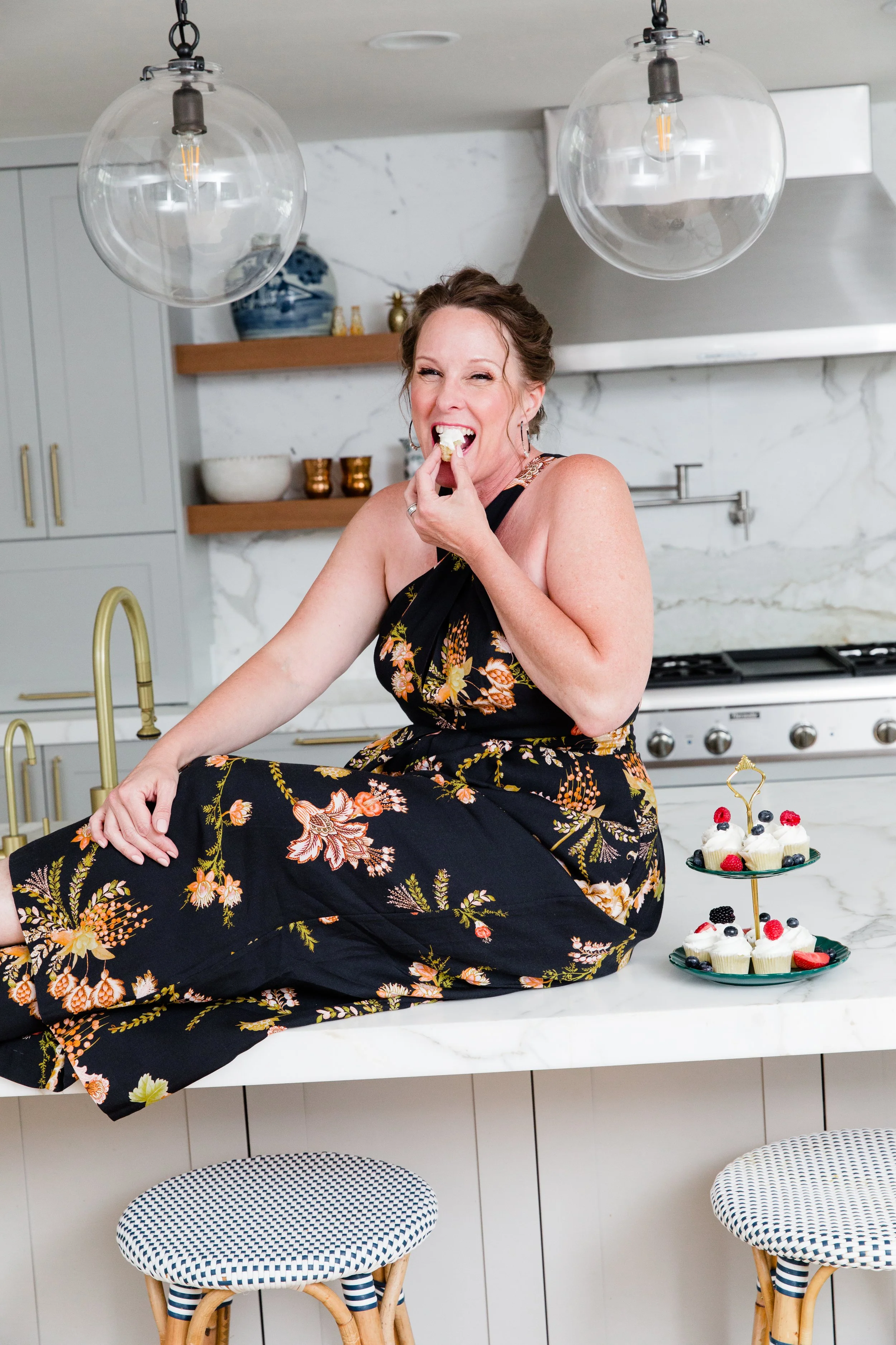 A woman in a black floral dress sits on a marble kitchen counter, smiling as she enjoys a dessert. This image reflects a grounded, joyful relationship with food central to eating disorder therapy in Olympia, WA.