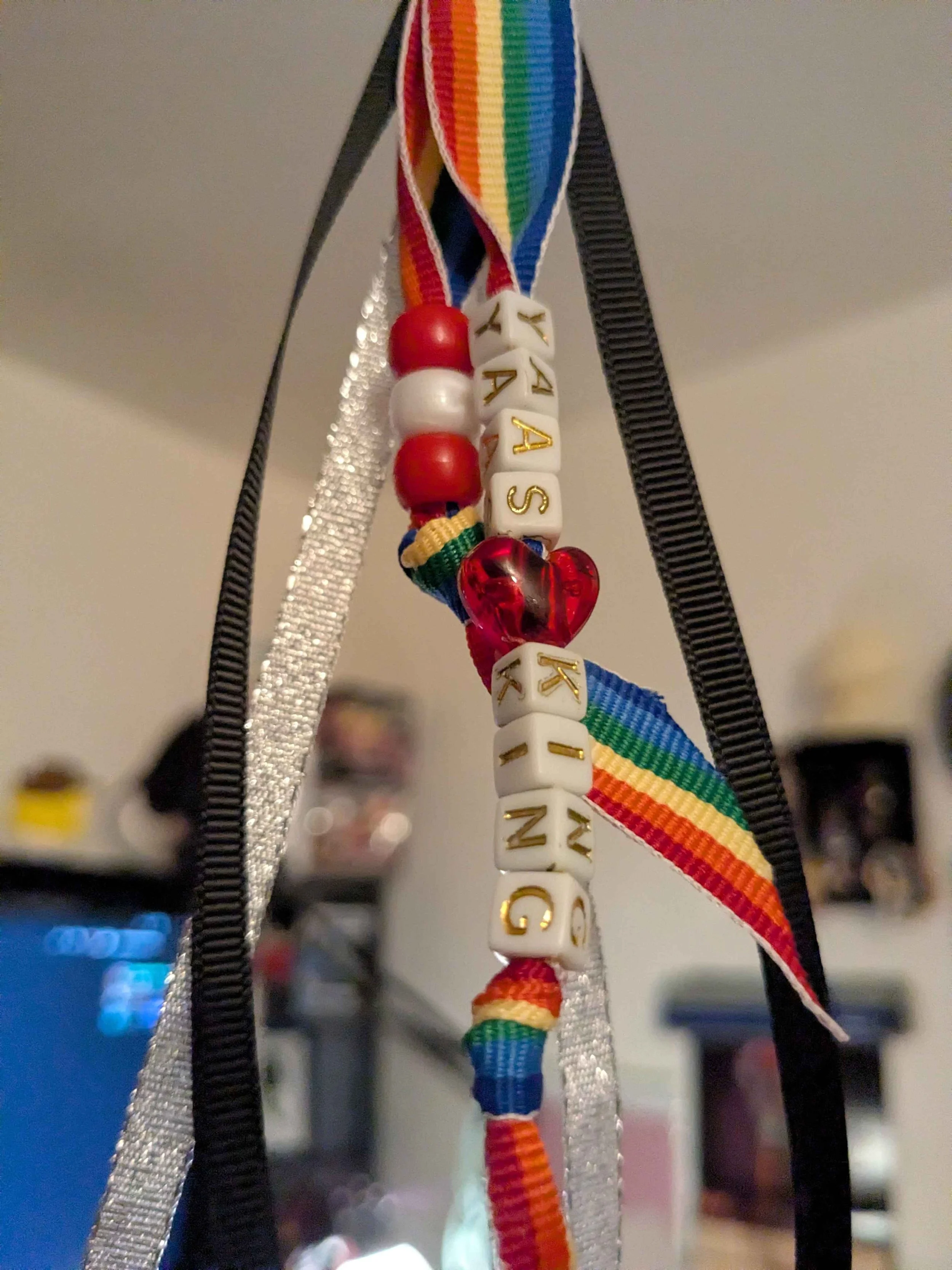 detail zoomed in image of a pride keychain with ribbon tassels hanging down.  The plastic beads spell out "Yaas King" with a heart between the words