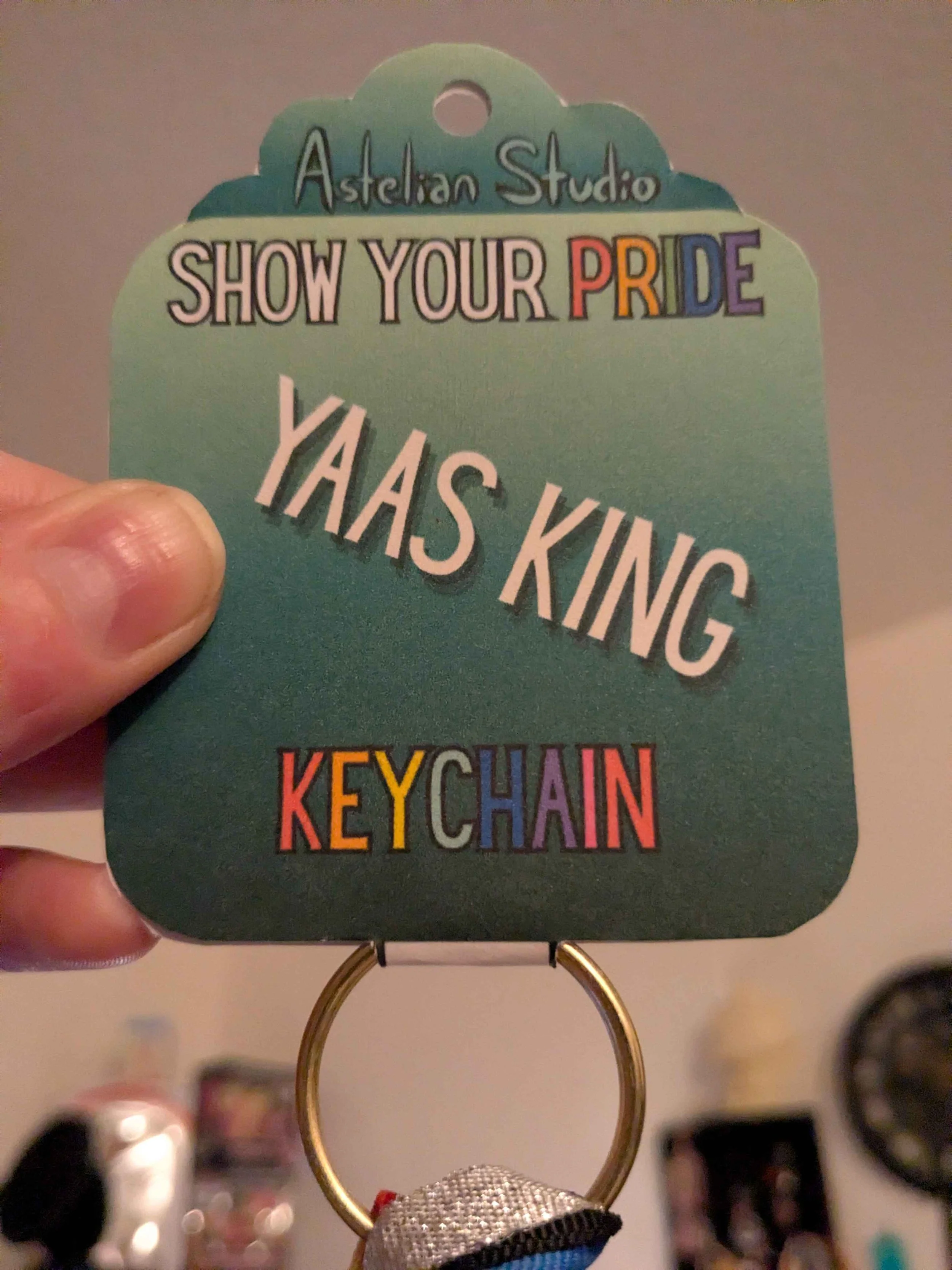 detail picture of a light skinned hand holding up a priduct info card for a pride keychain made by Astelian Studio