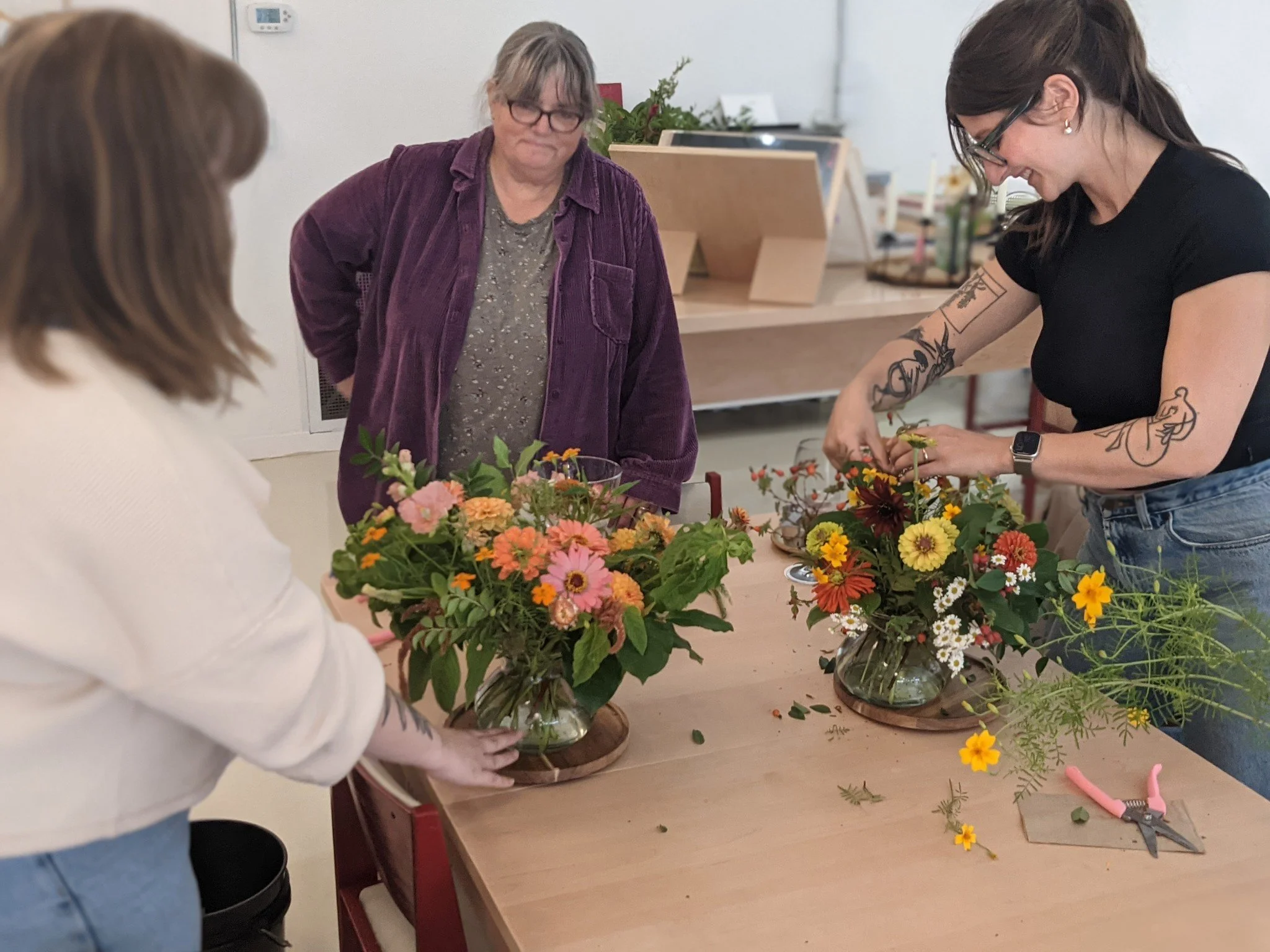 People gathered around a table arranging colorful flower bouquets in glass vases.