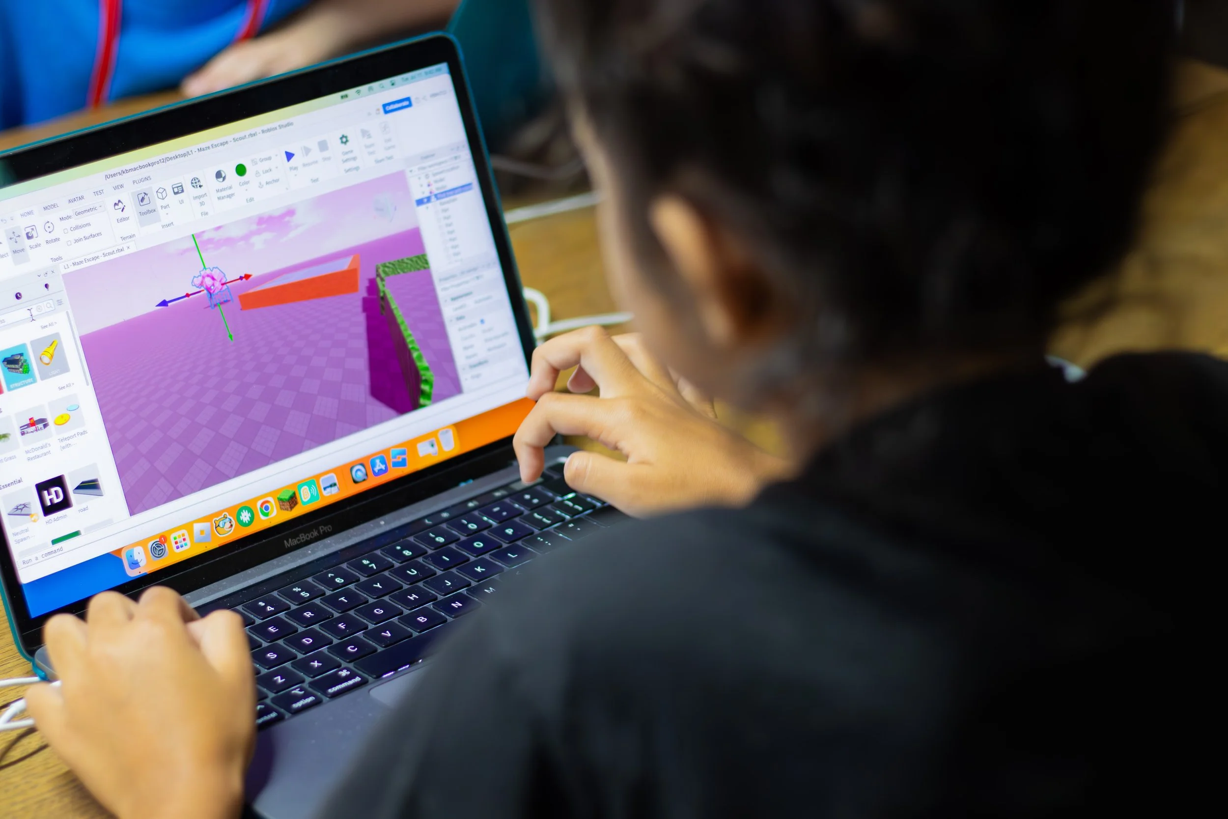 A person working on a laptop with a 3D modeling or game development software open on the screen.