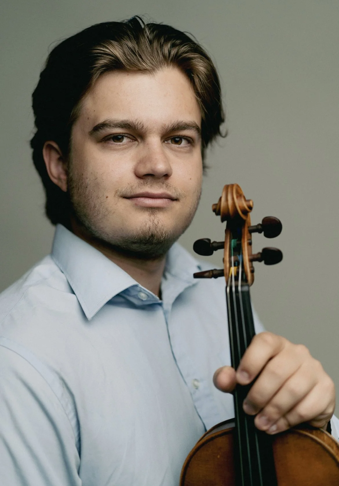 En ung mann med skallet hår holder en fiolin og ser mot kamera.