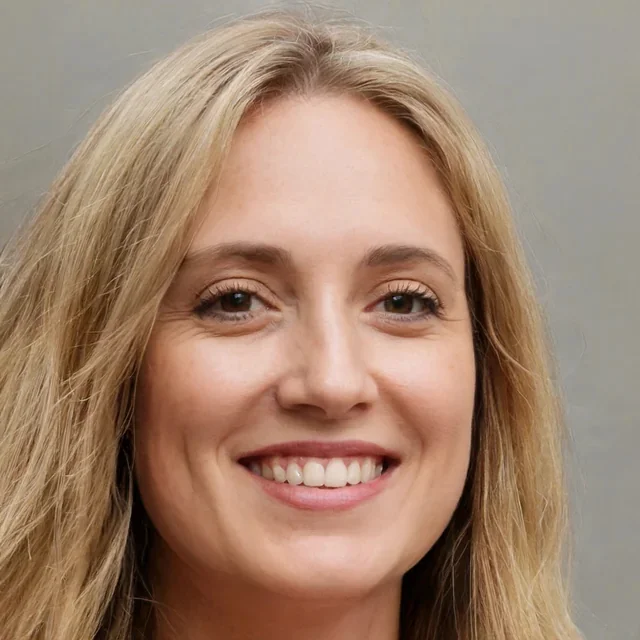 Close-up of a smiling woman with blonde hair and light makeup against a plain background.
