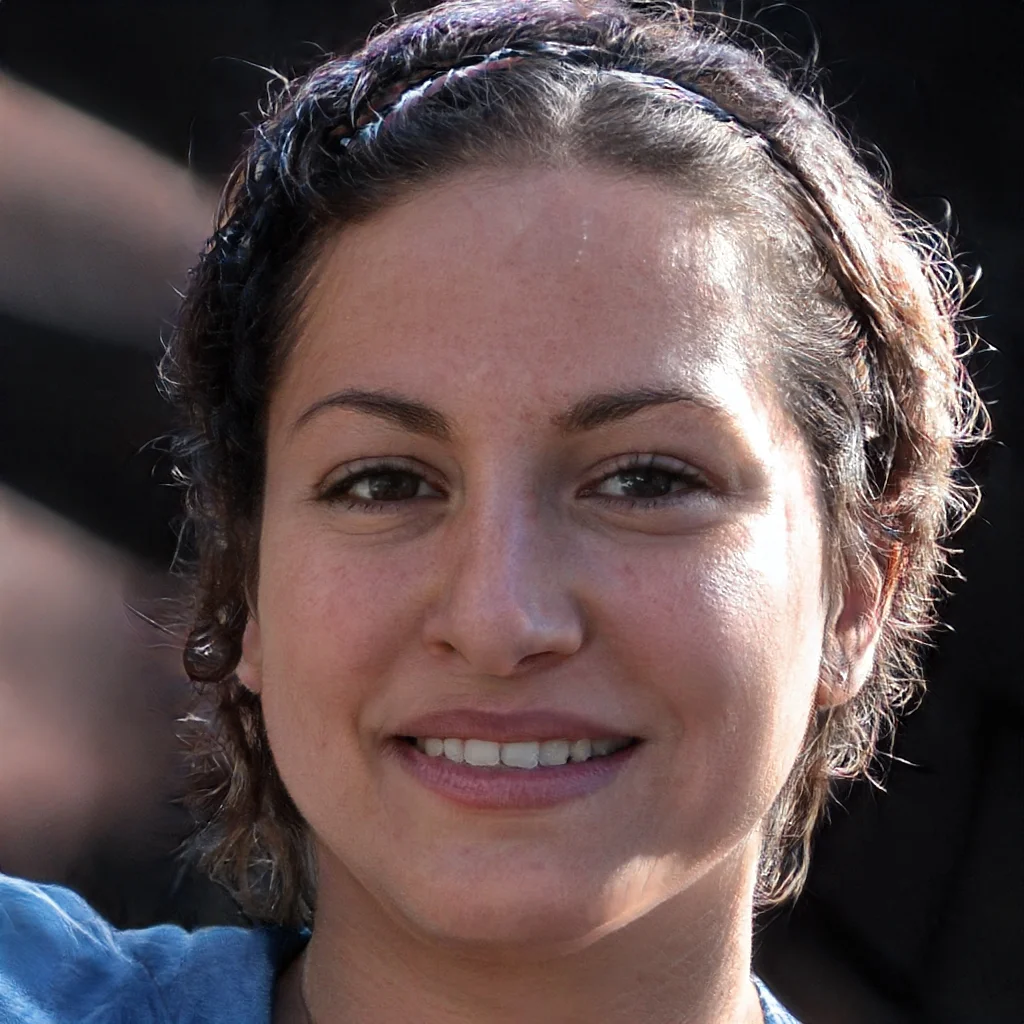 Close-up of a young woman with short, curly hair and a black headband, smiling outdoors in sunlight.