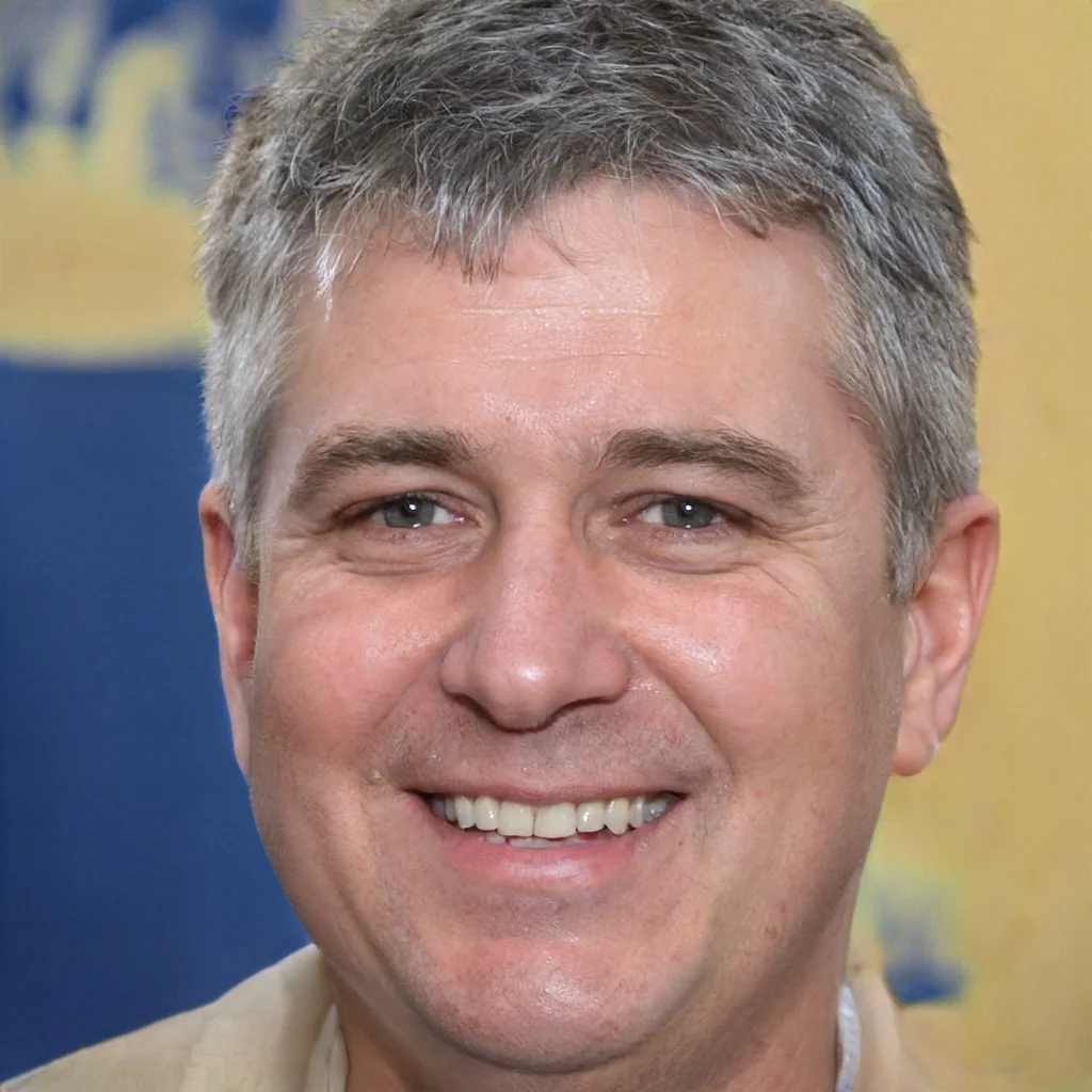 Close-up of a smiling middle-aged man with short gray hair, blue eyes, and light skin, wearing a beige suit jacket, in front of a background with blue and yellow colors.