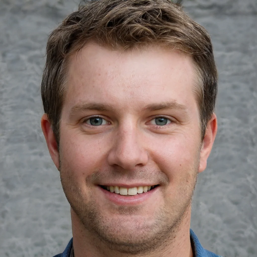 Close-up of a young man with short brown hair and blue eyes smiling in front of a gray textured background.