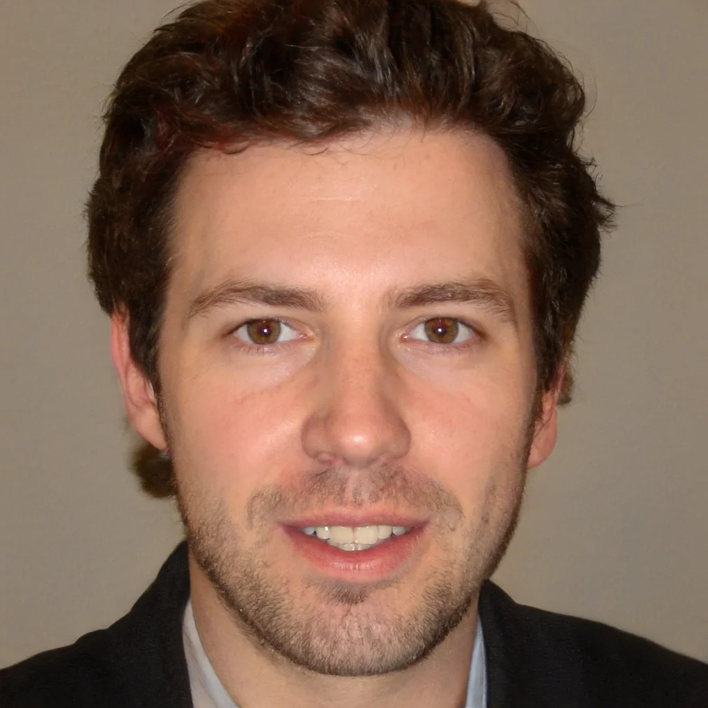 Close-up of a man with wavy brown hair, hazel eyes, and light skin, smiling at the camera, wearing a black suit jacket.