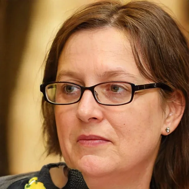 Close-up of a woman with glasses and earrings, looking to the side in a thoughtful expression.