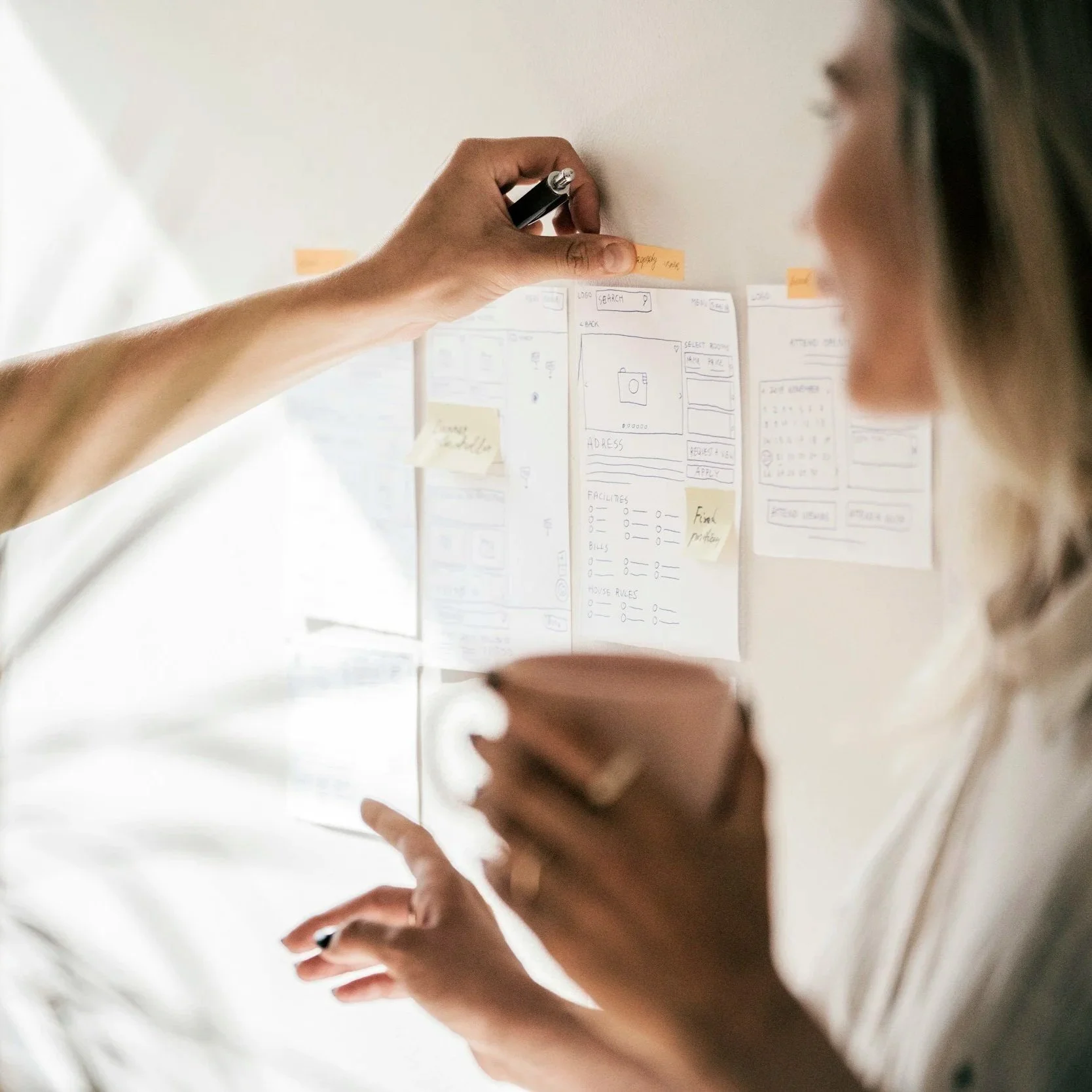 Two women working on a whiteboard with sketches and notes for a mobile app design.
