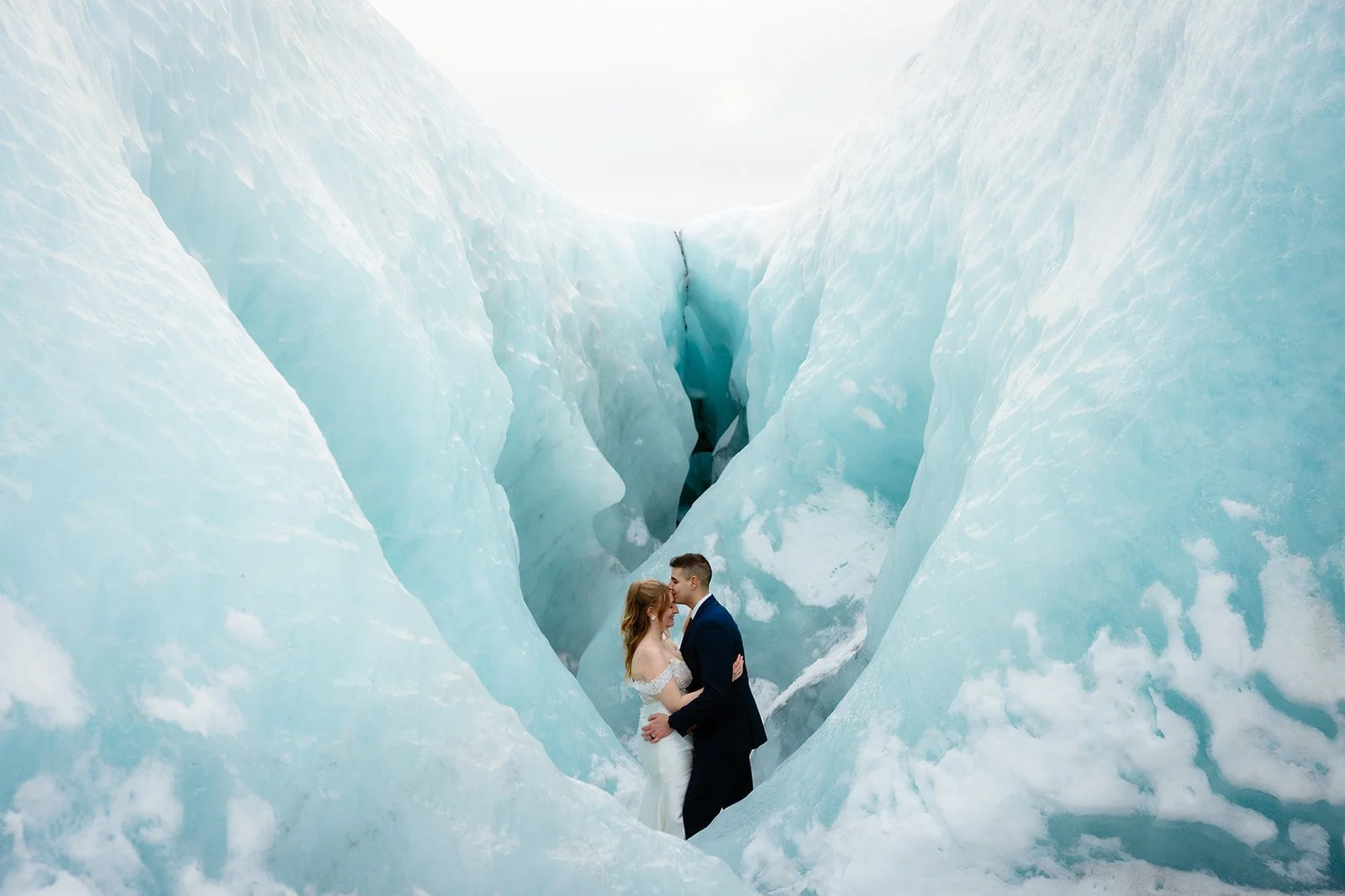 A couple in wedding attire sharing a kiss in a crevice of large blue glaciers in Iceland during elopement.