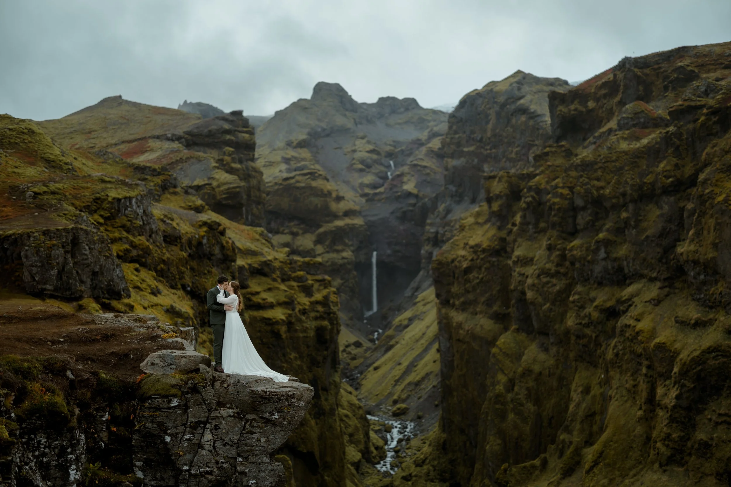 bride and groom kiss while standing on a ledge during iceland elopement