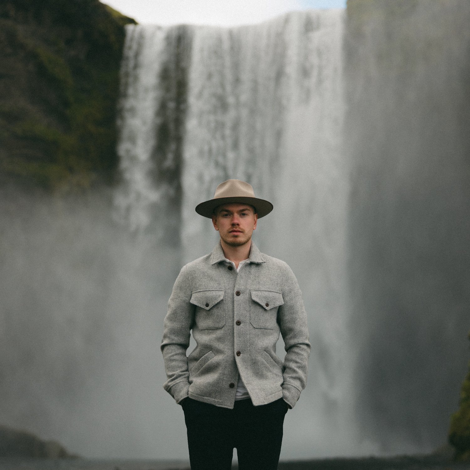 iceland wedding photographer stands in front of waterfall