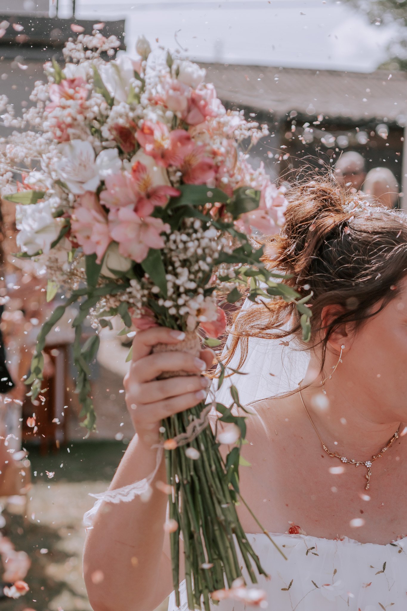 Bride holding a bouquet of pink and white flowers during a celebration with falling flower petals.