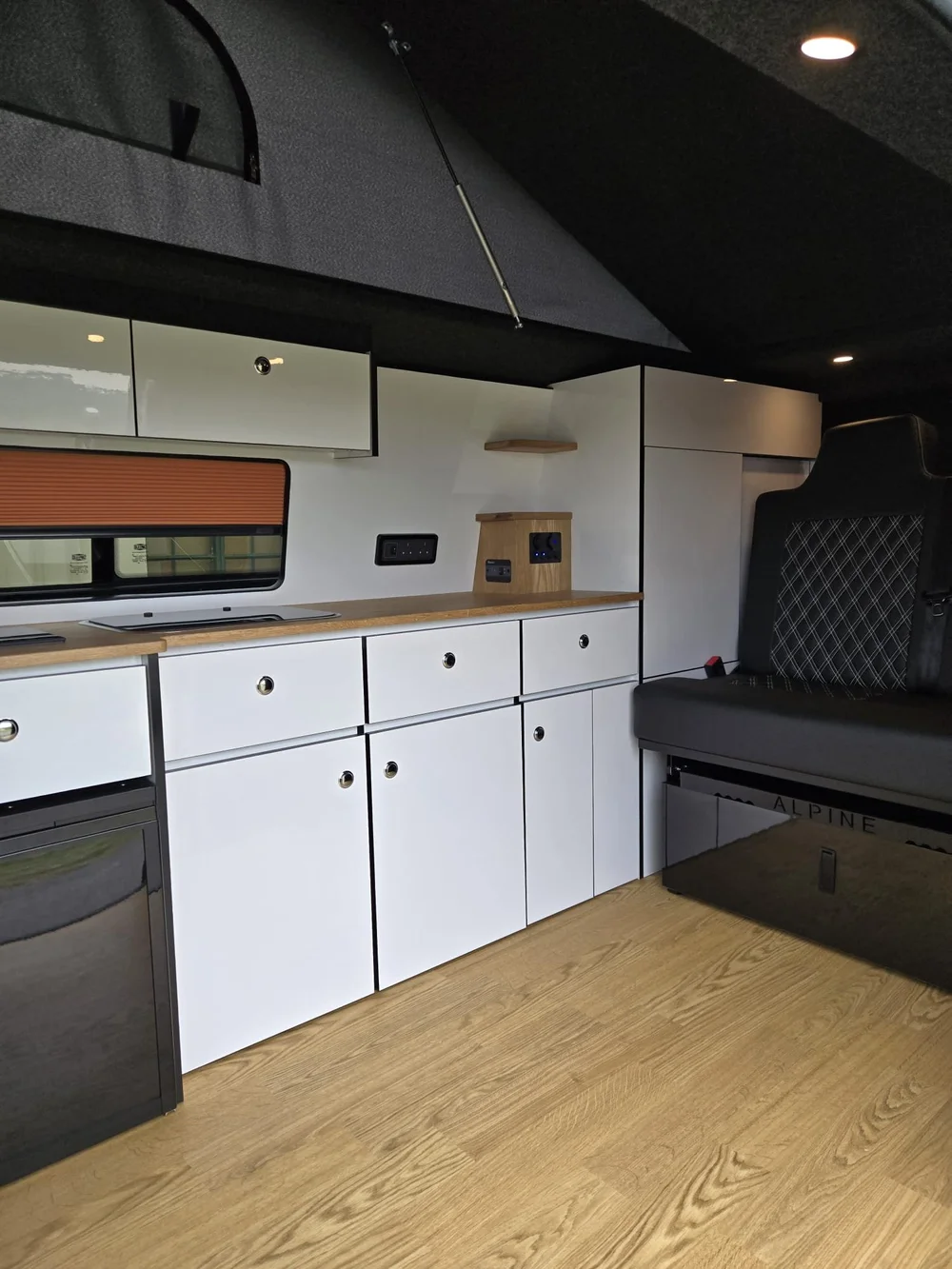 Bespoke kitchen cabinets in a VW T6.1 camper conversion by Grizzly Custom Vans with white gloss units and oak worktops