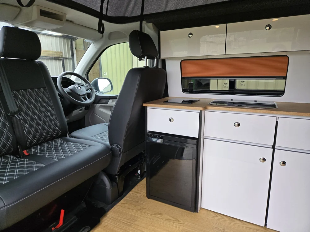 Interior of a VW T6.1 camper conversion by Grizzly Custom Vans with bespoke white cabinetry and oak worktops