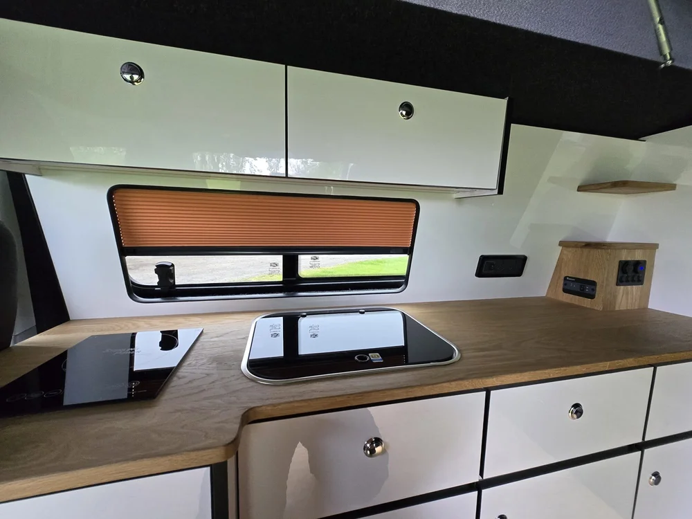 Custom VW van kitchen featuring induction hob, sink, fridge, and modern storage in a VW T6.1 camper