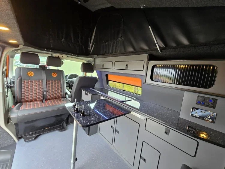 Campervan interior featuring custom upholstery alongside fitted kitchen units and storage.