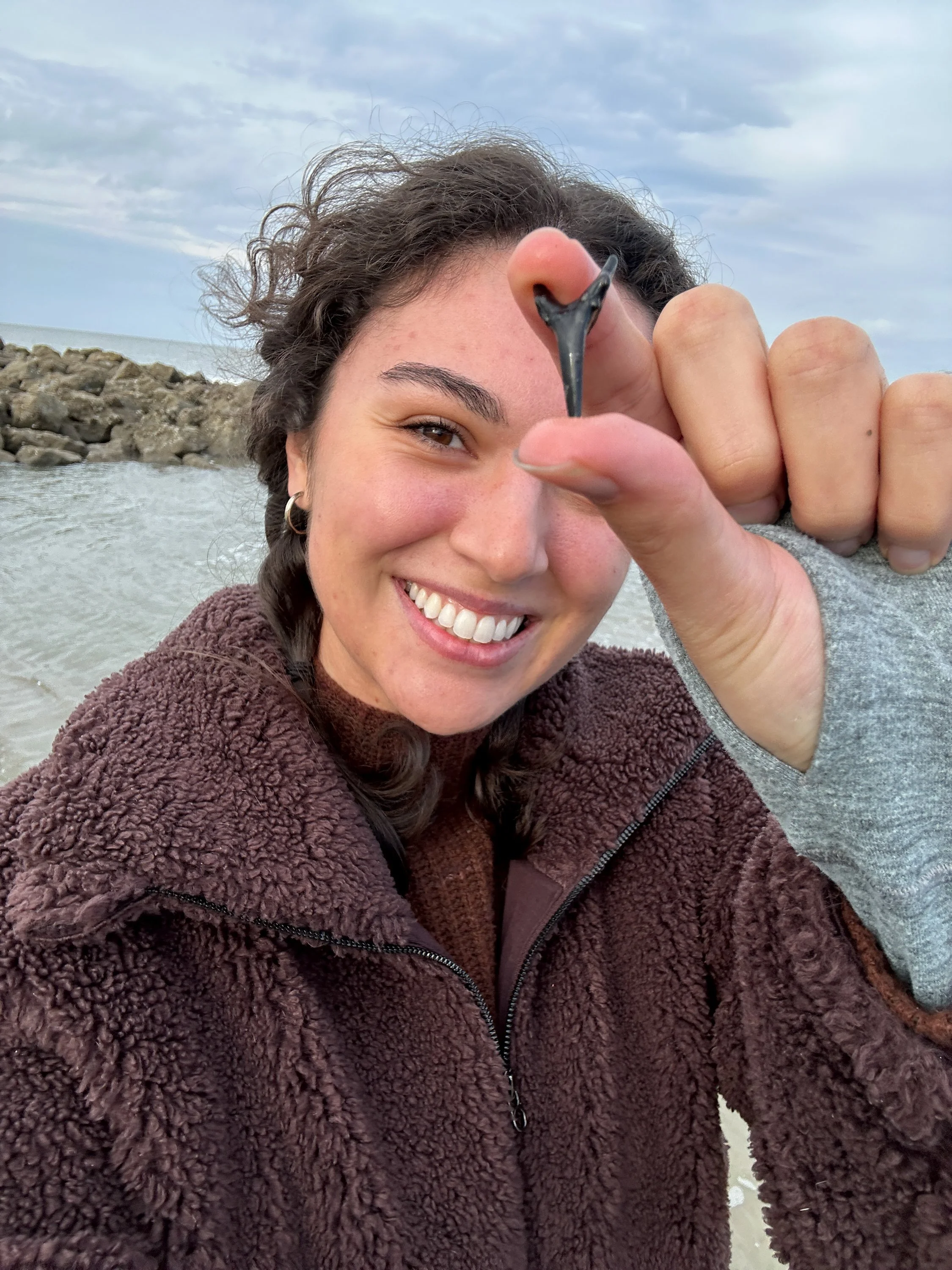 A young woman is smiling and holding a small fish with her right hand at the beach.