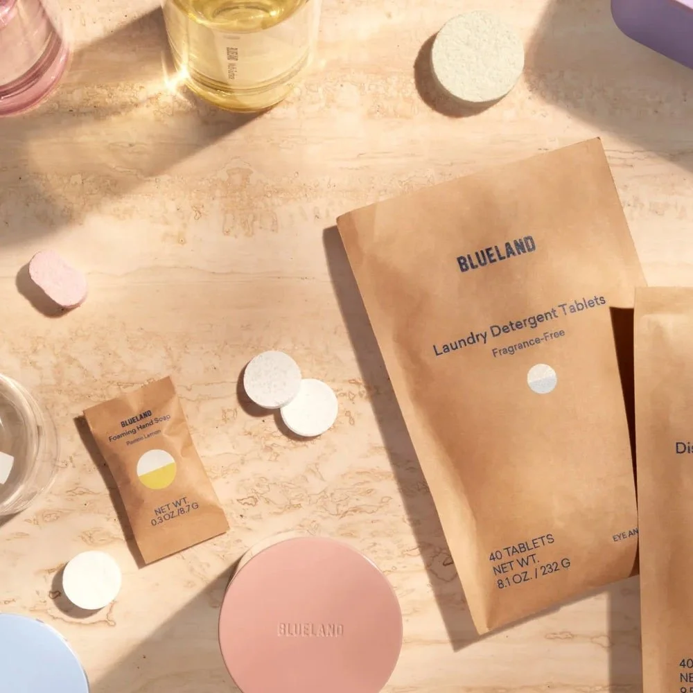 Flat lay of laundry detergent tablets, hand soap, and skincare products on a wooden surface.
