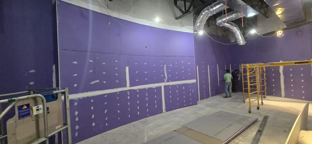 Construction workers painting purple walls with drywall joint compound in an interior space under construction.