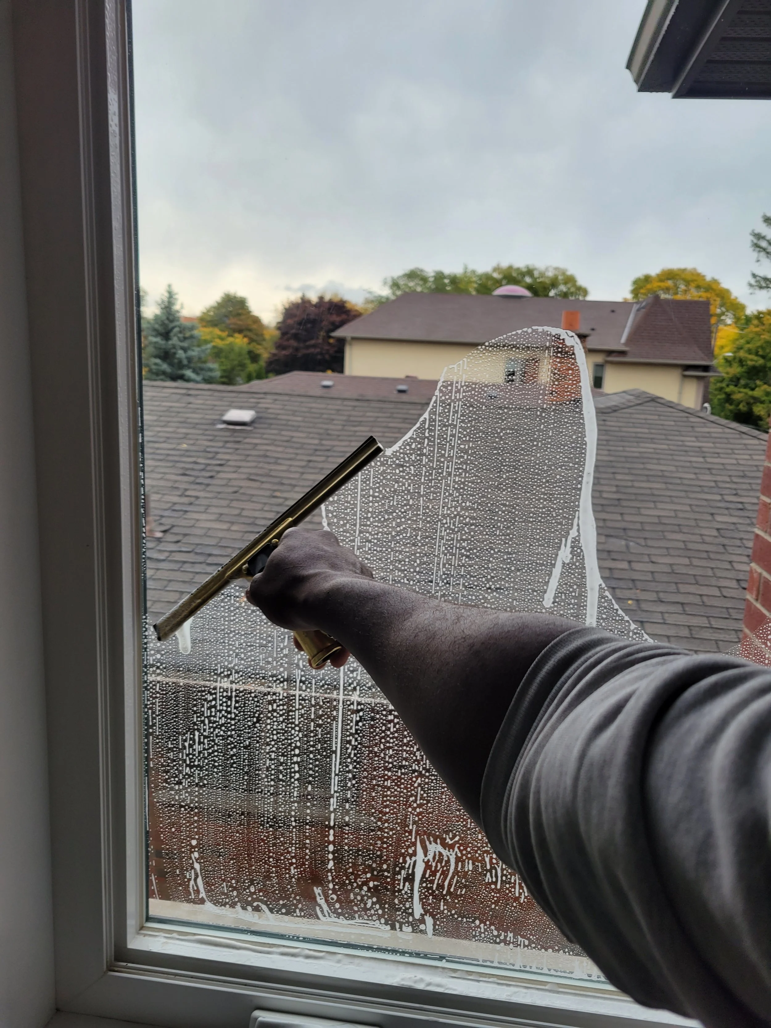 Person cleaning a window from inside the house, using a squeegee to remove soapy water.