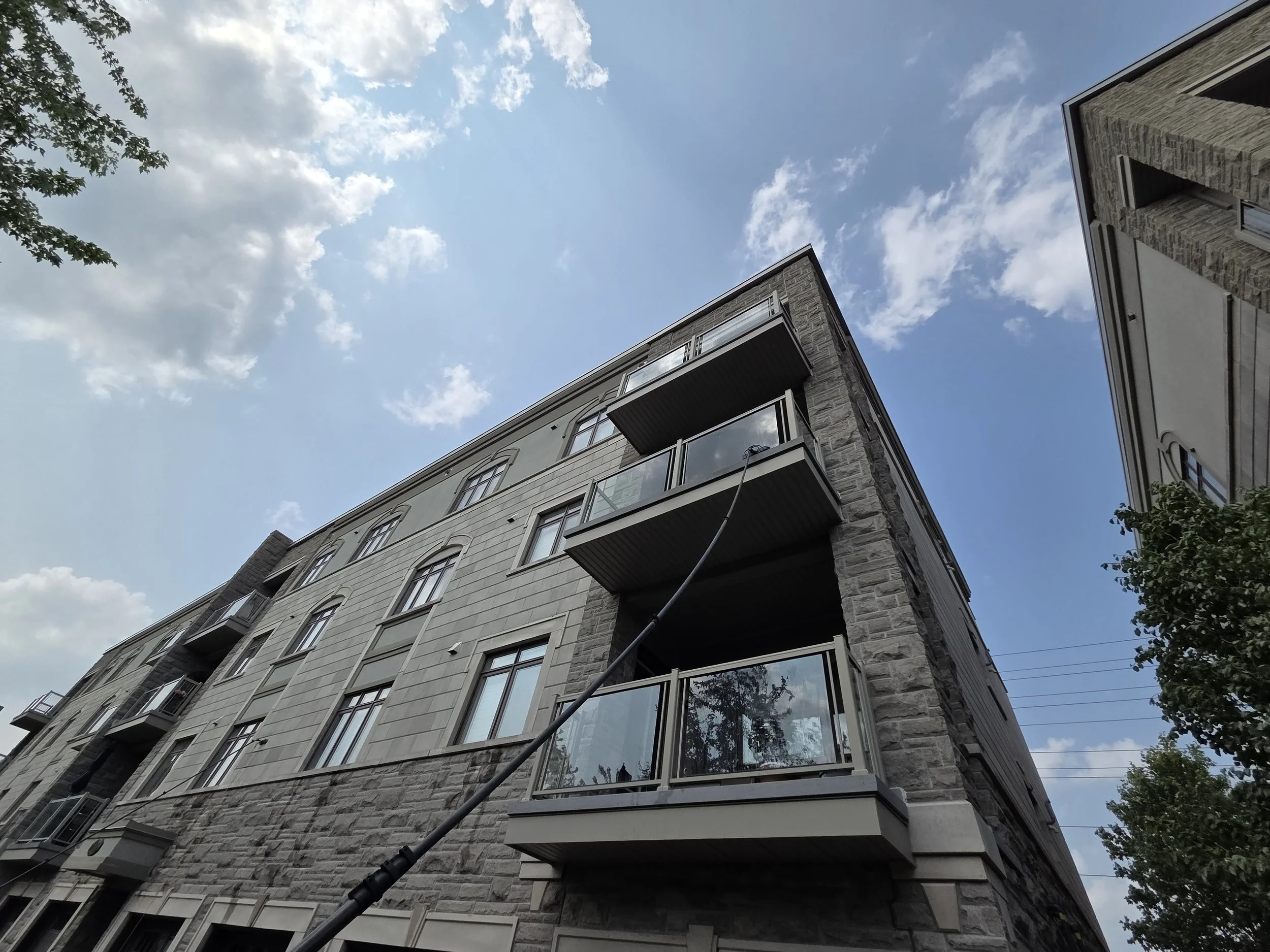 Low-angle view of an apartment building with balconies, against a partly cloudy blue sky.
