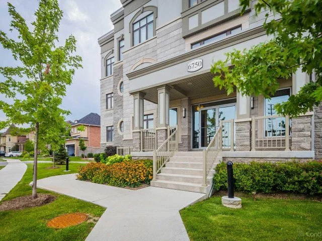 Front entrance of a modern apartment building with steps, nearby trees, and landscaped bushes.