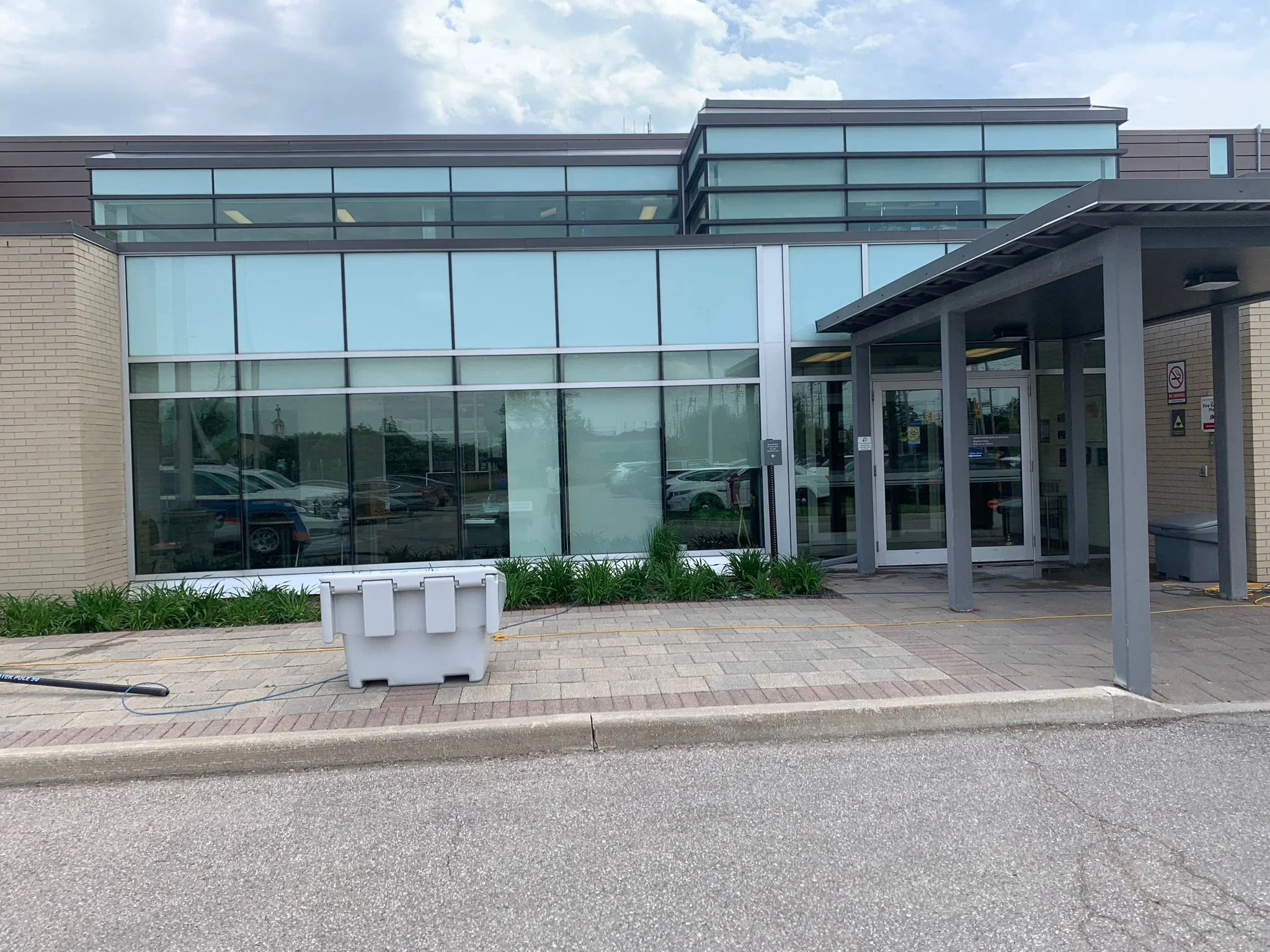 Exterior of a modern office building with large glass windows, a covered entrance, and a few parked cars visible through the windows.