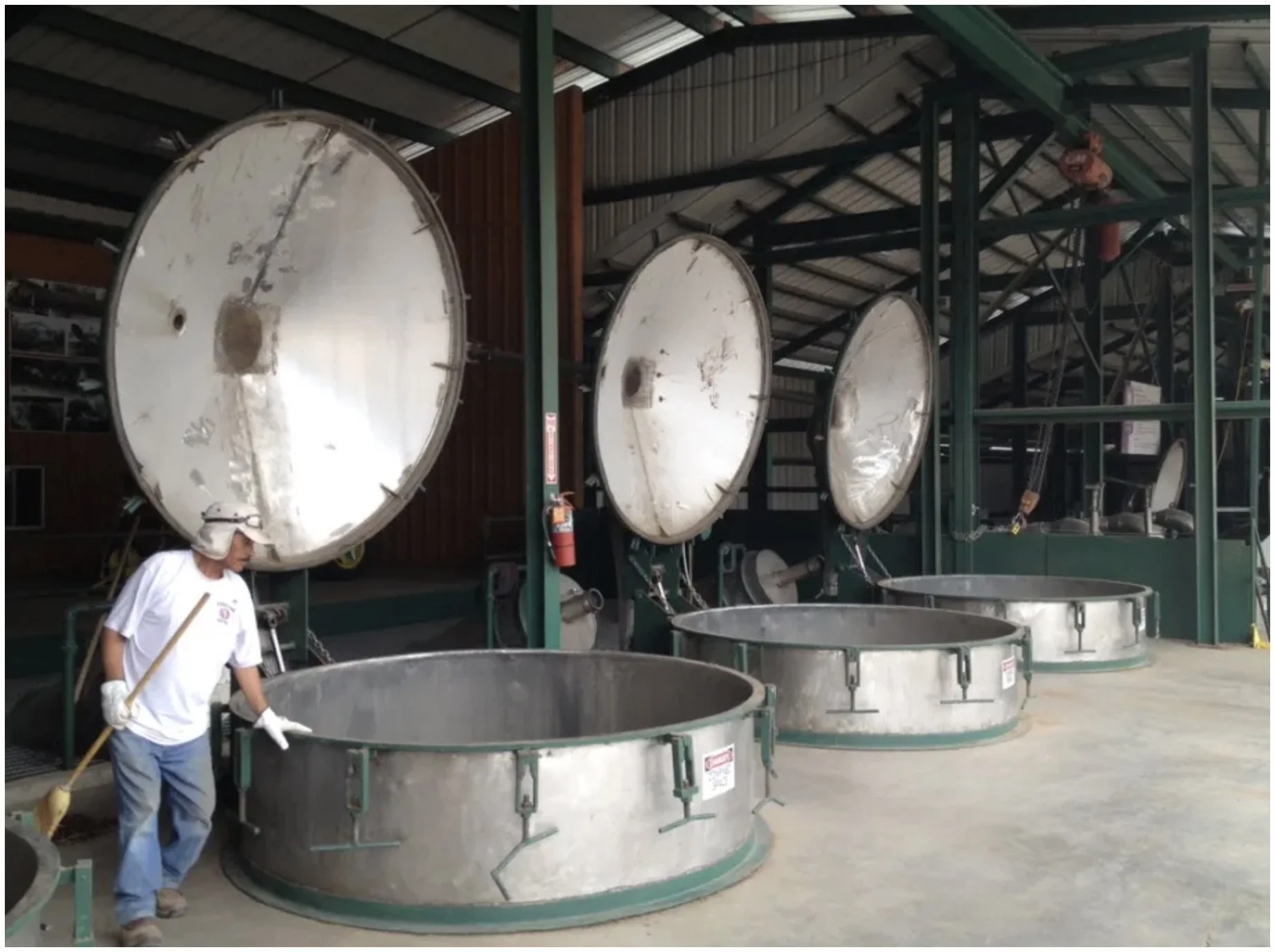 Large industrial centrifuges inside a factory, with a worker cleaning one of the machines, wearing safety gloves, a hat, and a white shirt.