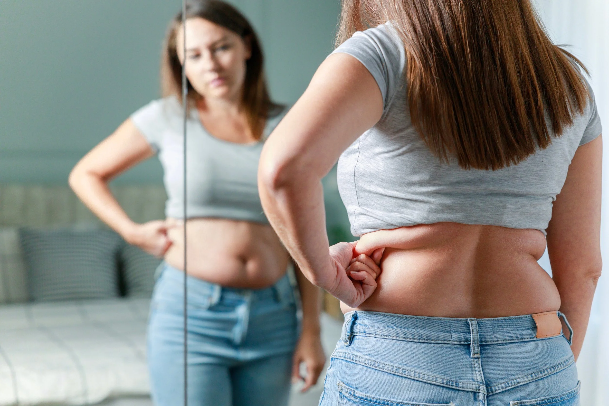 Woman looking in the mirror, grabbing belly fat