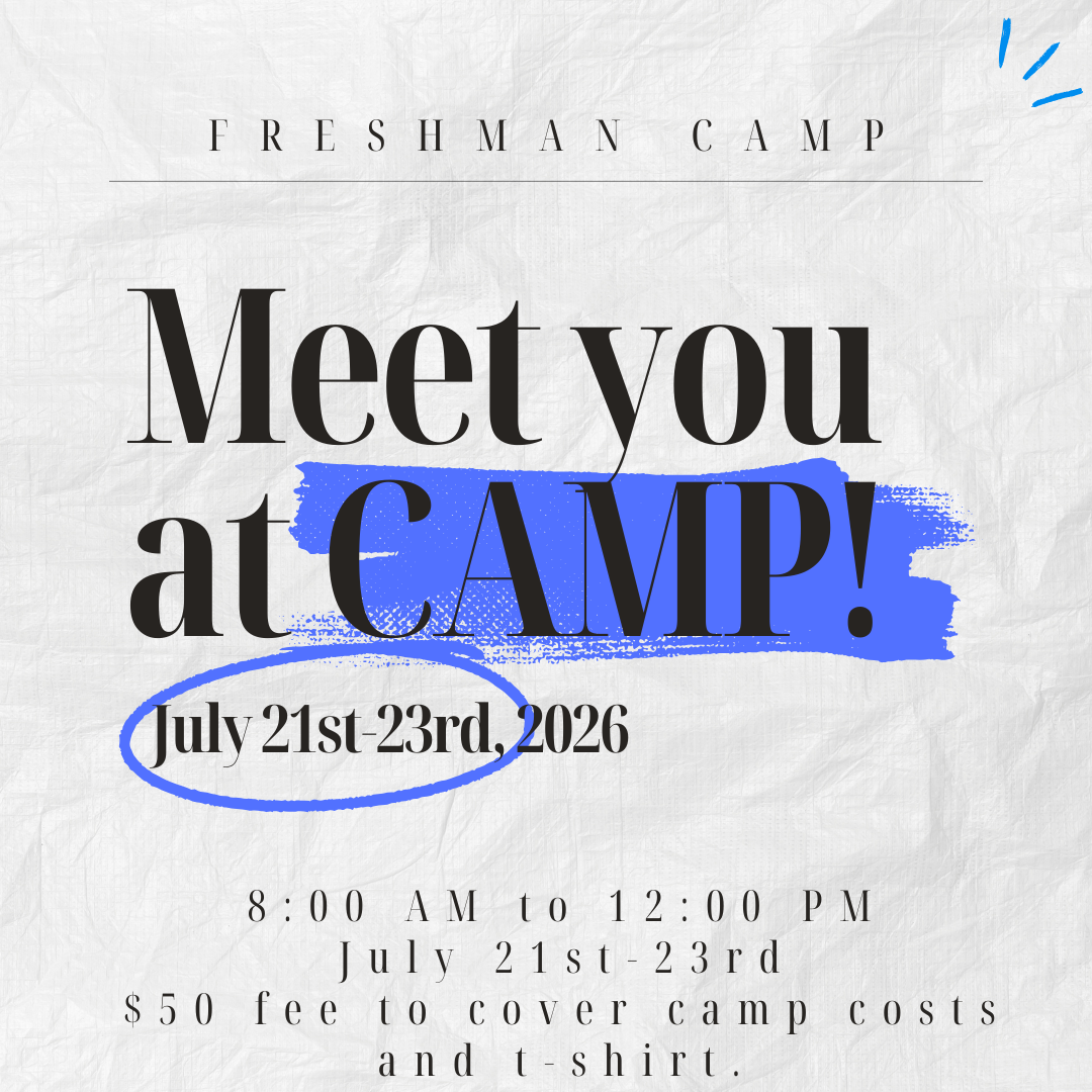 Group of young female volleyball players in blue jerseys posing for a team photo inside a gymnasium, with a volleyball net behind them and banners hanging on the walls.