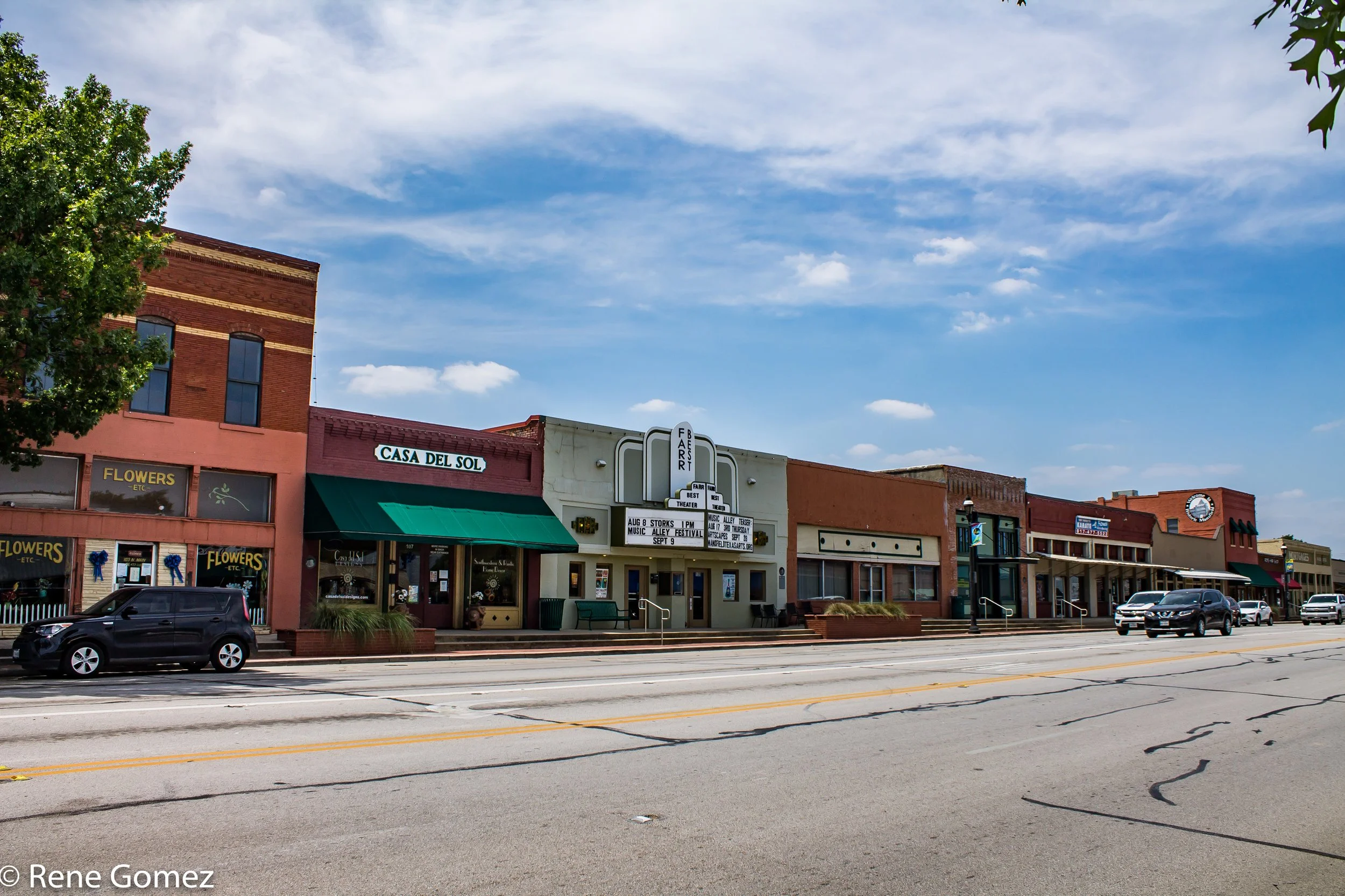 Street view of Mansfield, TX with storefronts and a theater. Buildings include Auto Glass Native, a flower shop, Casa Del Sol, and a theater with a marquee.