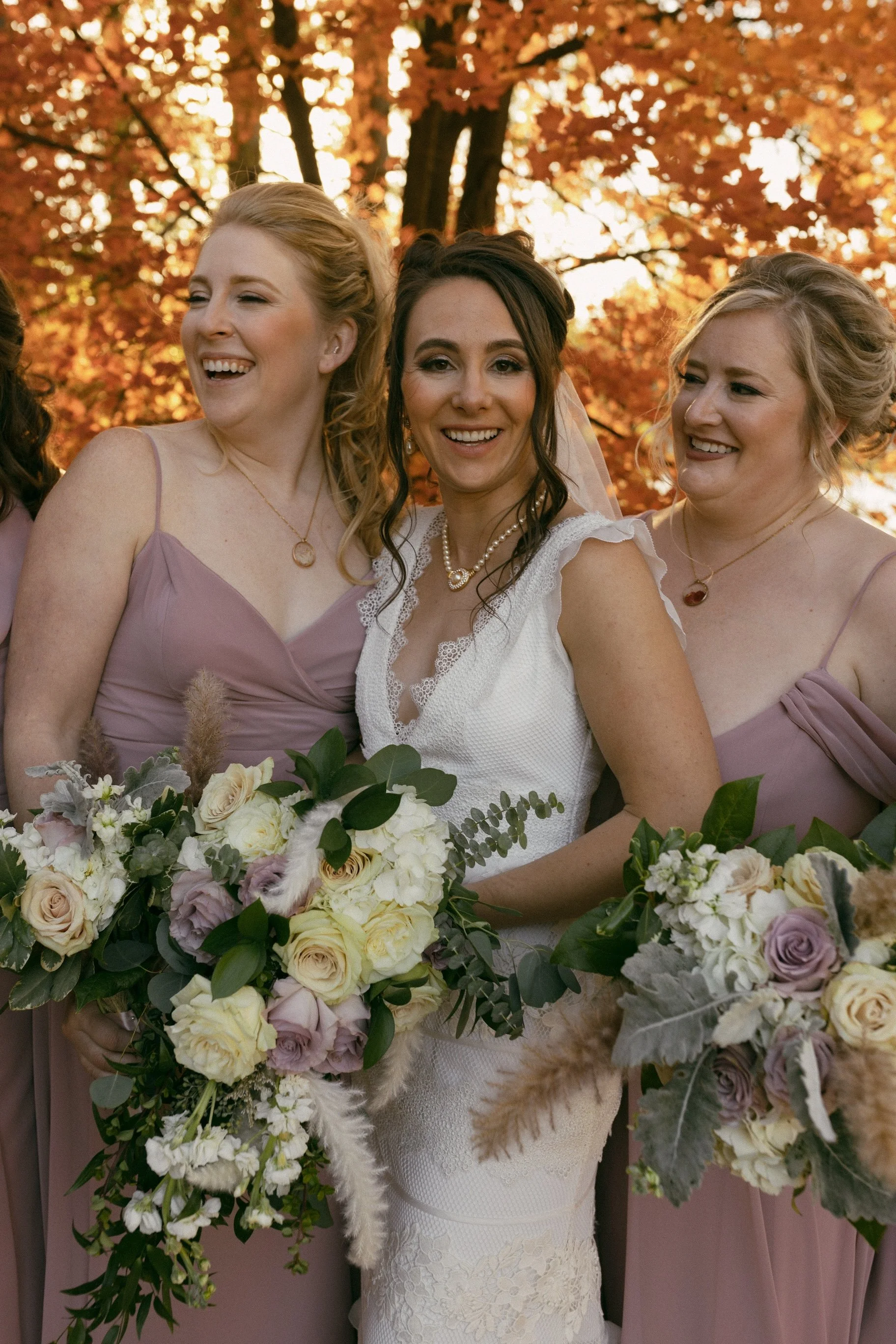 Nighttime outdoor dining table with white tablecloth, decorated with flowers, glasses, and bottles, illuminated by outdoor lighting, surrounded by trees and grass.