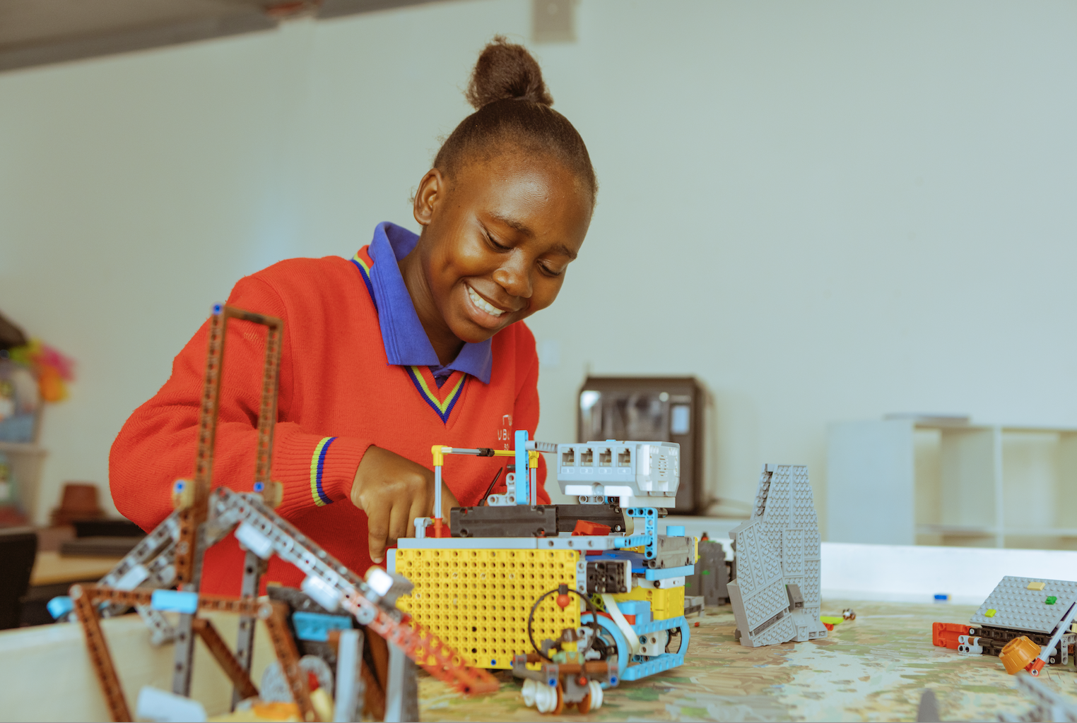 Young girl smiling and building a LEGO robot with various mechanical parts on a table.
