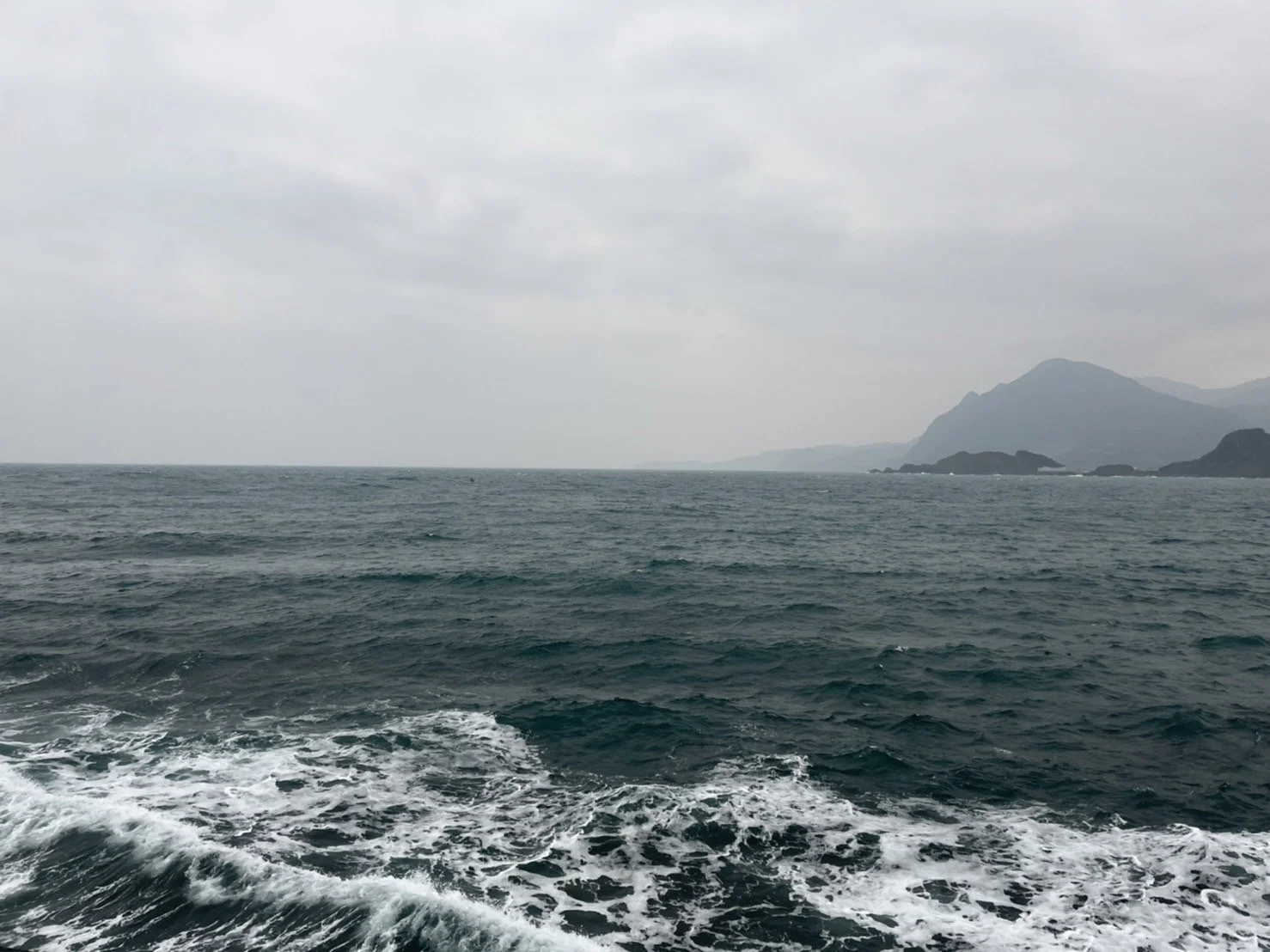 A view of the ocean with distant mountains and a cloudy sky.