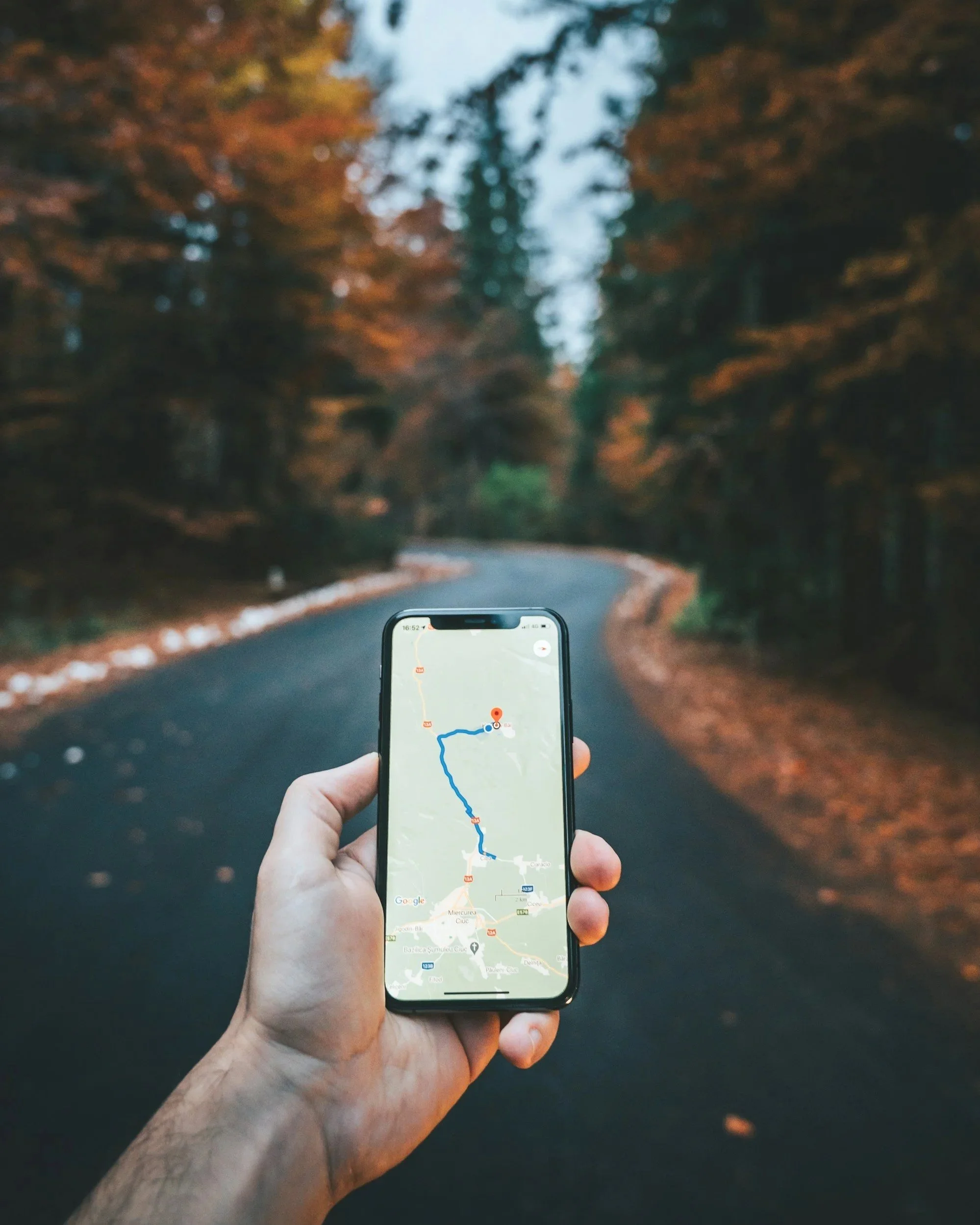 A person holding a phone with a map displayed on it.  A blacktop road is in the background.