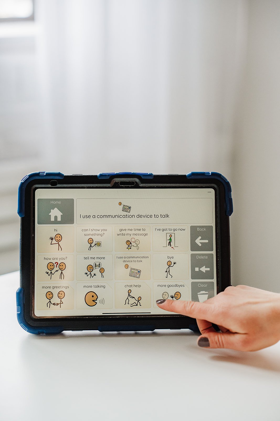 An augmentative and alternative communication (AAC) device is displayed.  A person is pointing to the button that says "I use a communication device to talk."