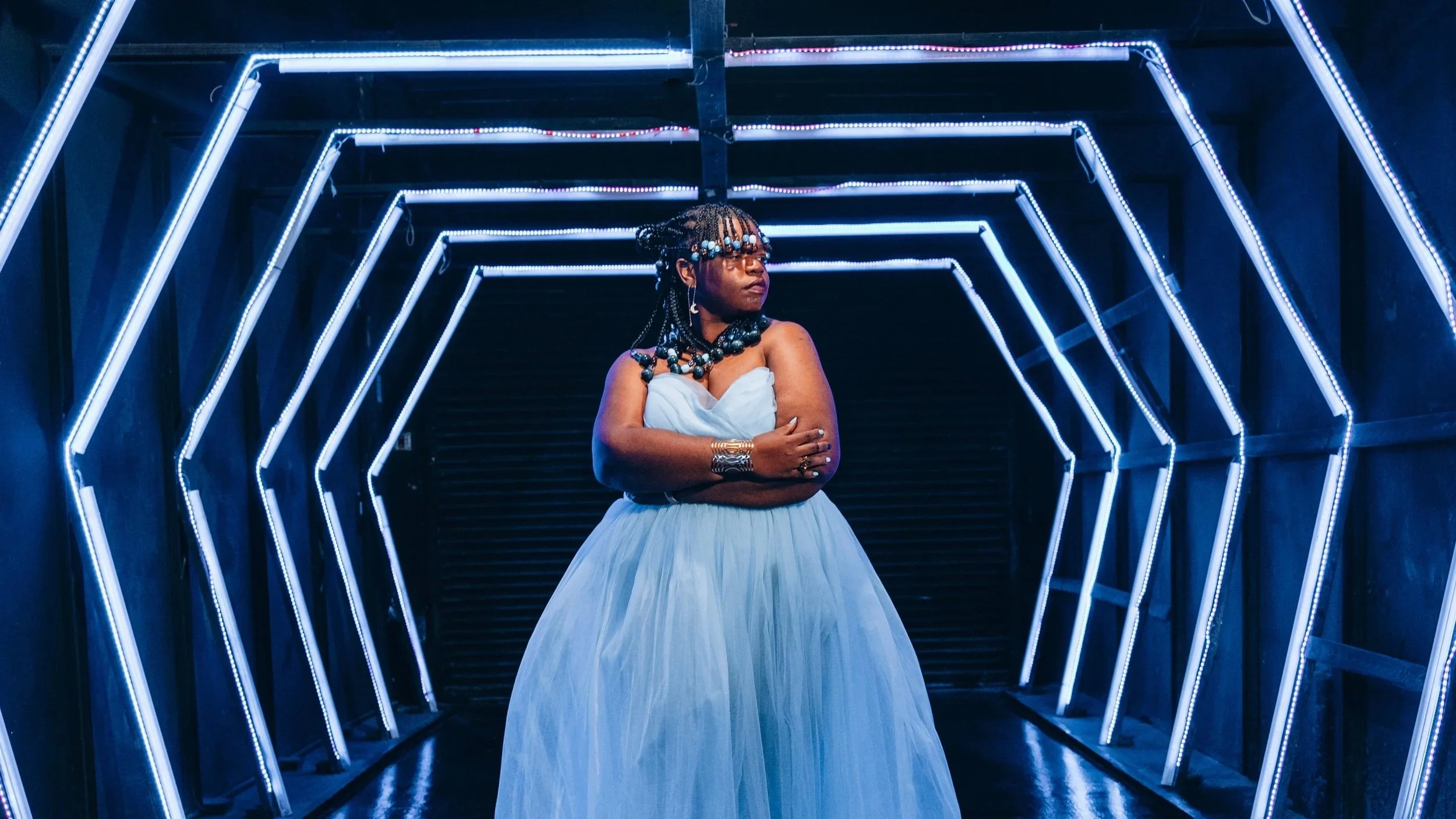 Dom Jones holds herself in a tunnel of bright blue light