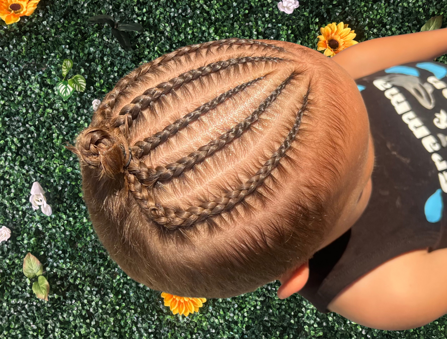 A child's head with long, blonde braids on a green leafy background with flowers.