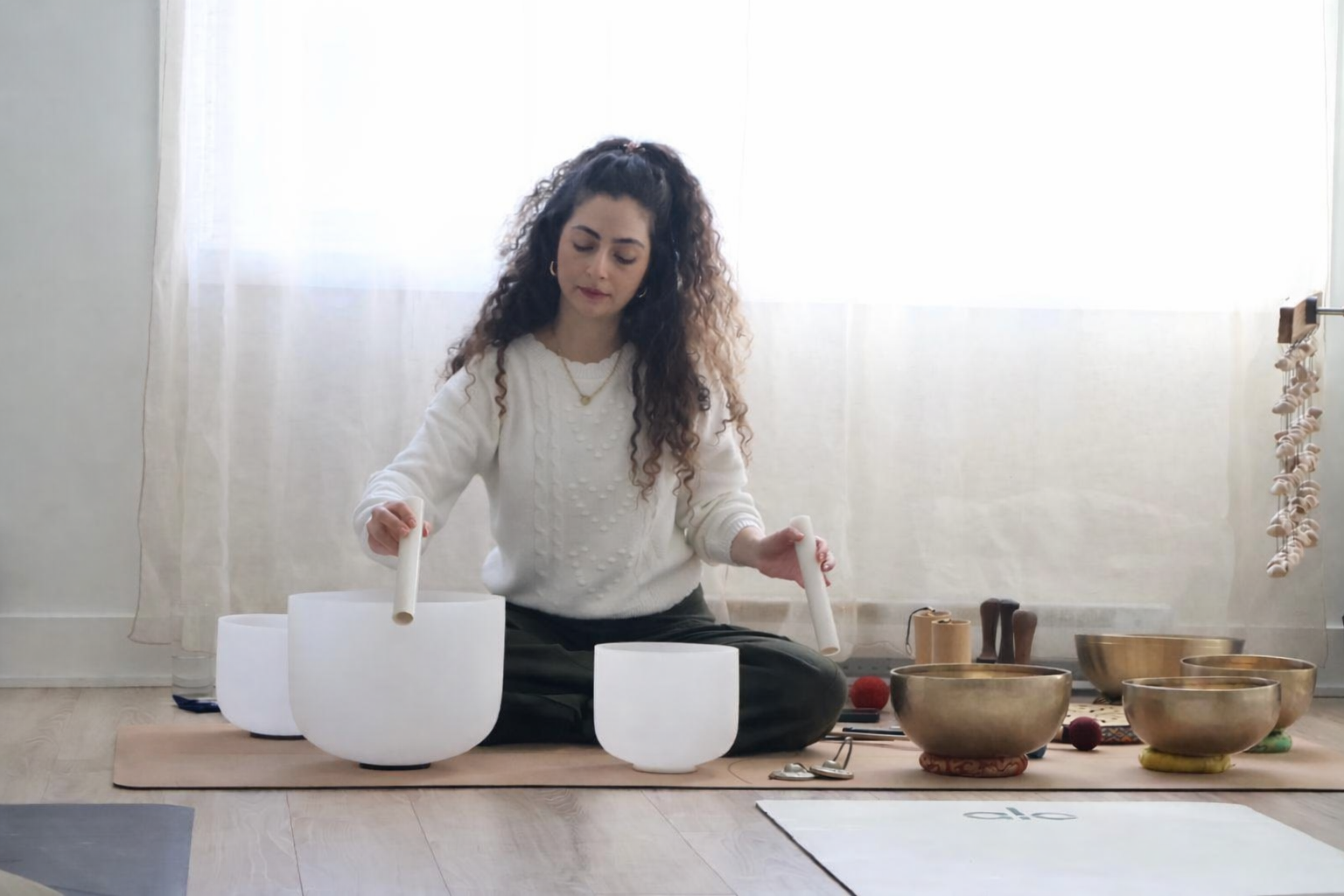 Woman sitting on the floor playing crystal singing bowls during a sound healing session.