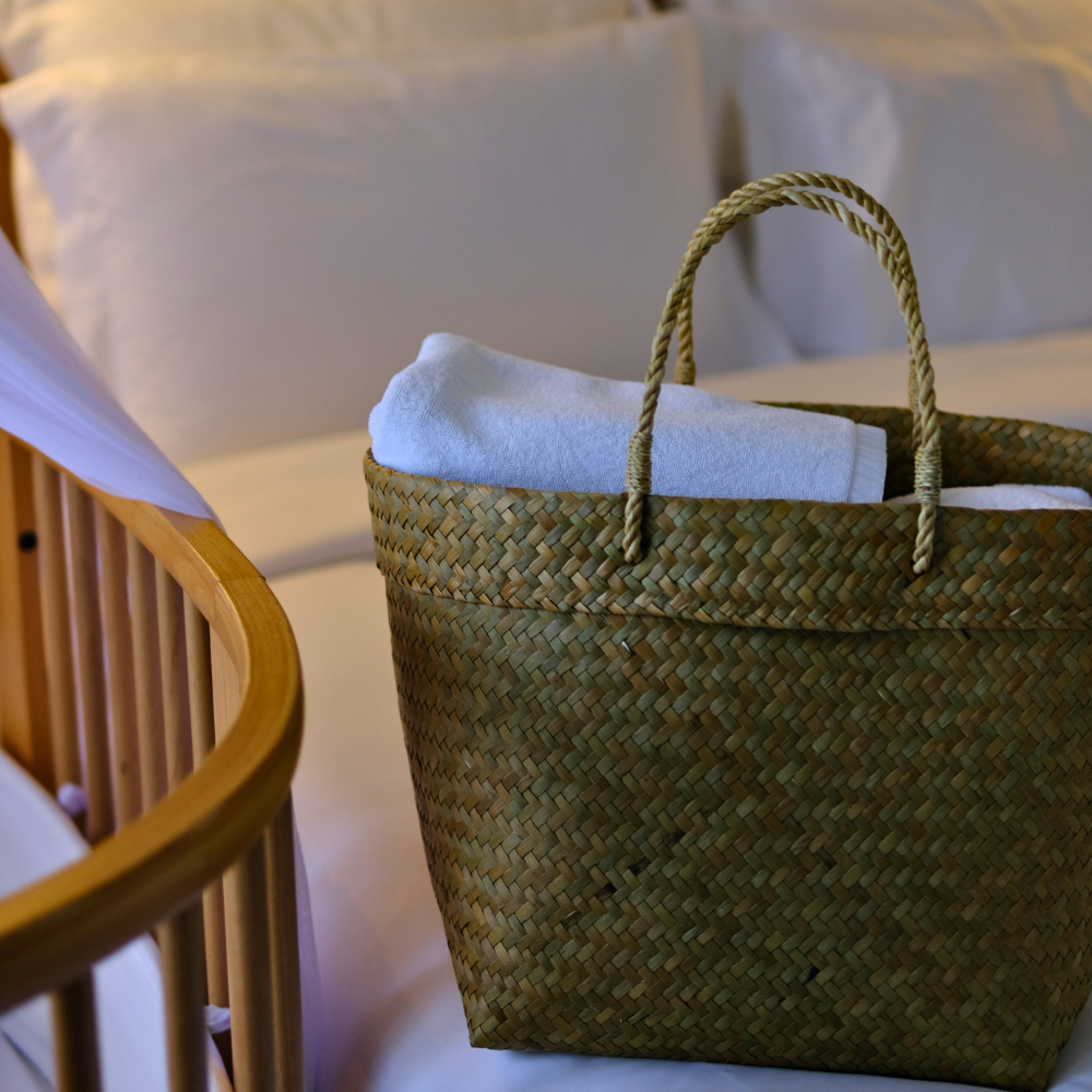 Tung Yai basket placed on a wooden bedside table next to a white bed, styled for calm bedroom storage.