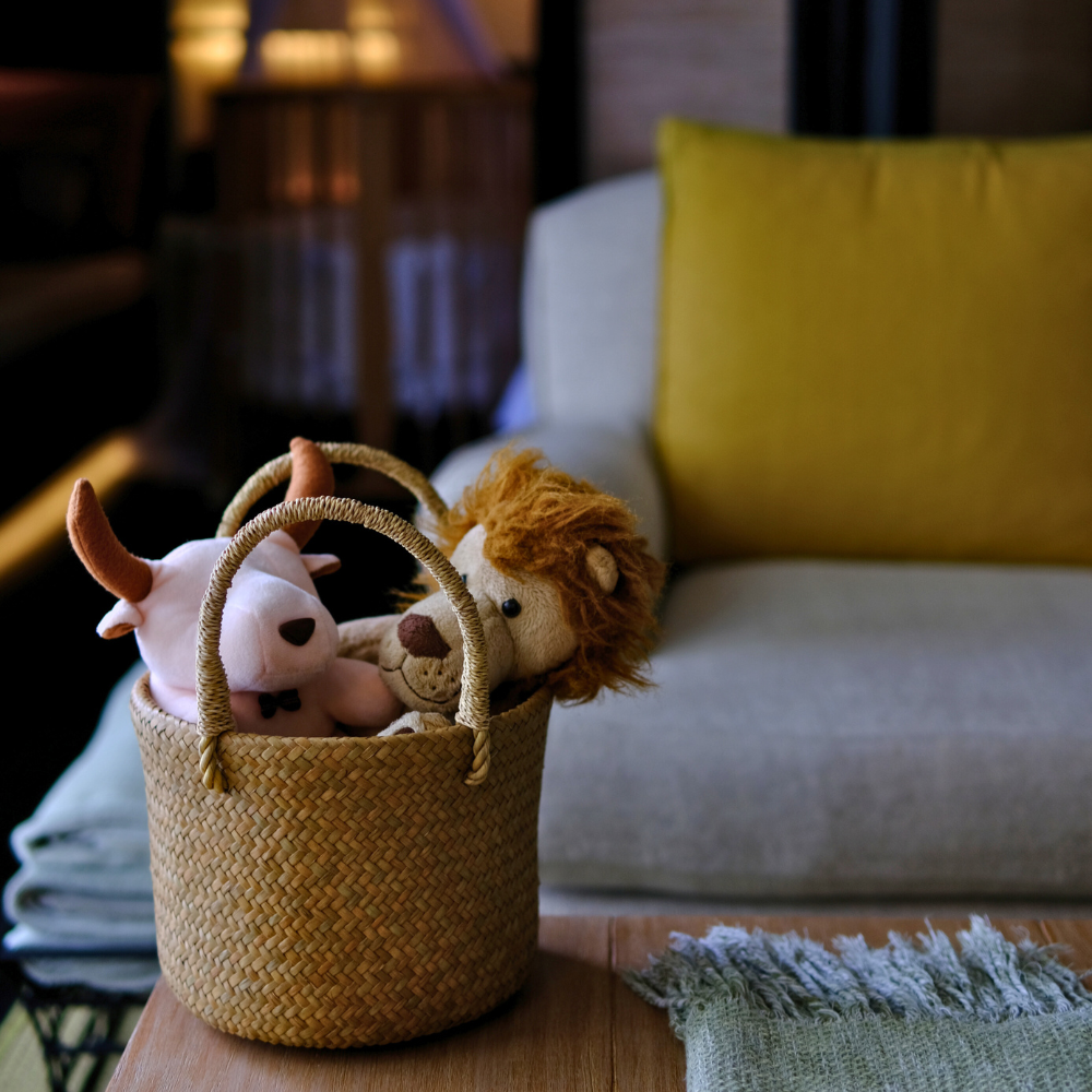 The Tung Dek basket by a low table under ambient lighting, styled with plush animals to convey warmth, texture, and function in evening settings.