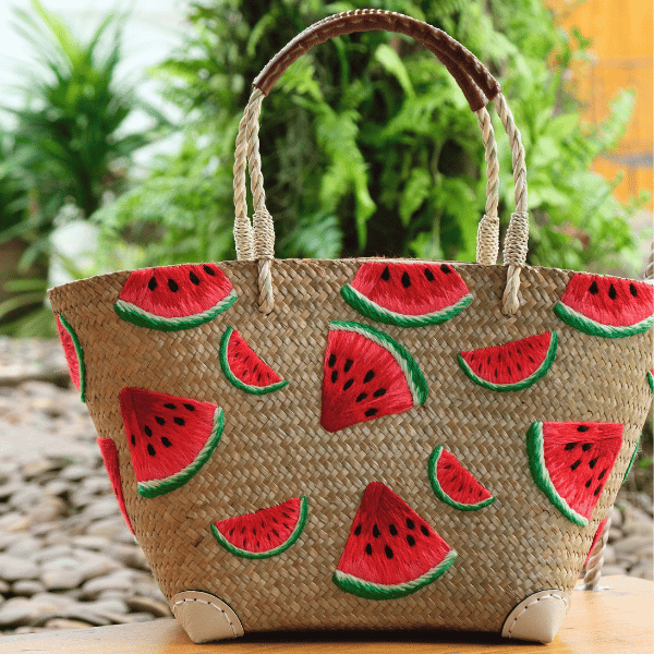 Watermelon Bites tote styled outdoors on a stone path with green foliage, emphasizing the vivid red embroidery and eco-friendly craftsmanship.